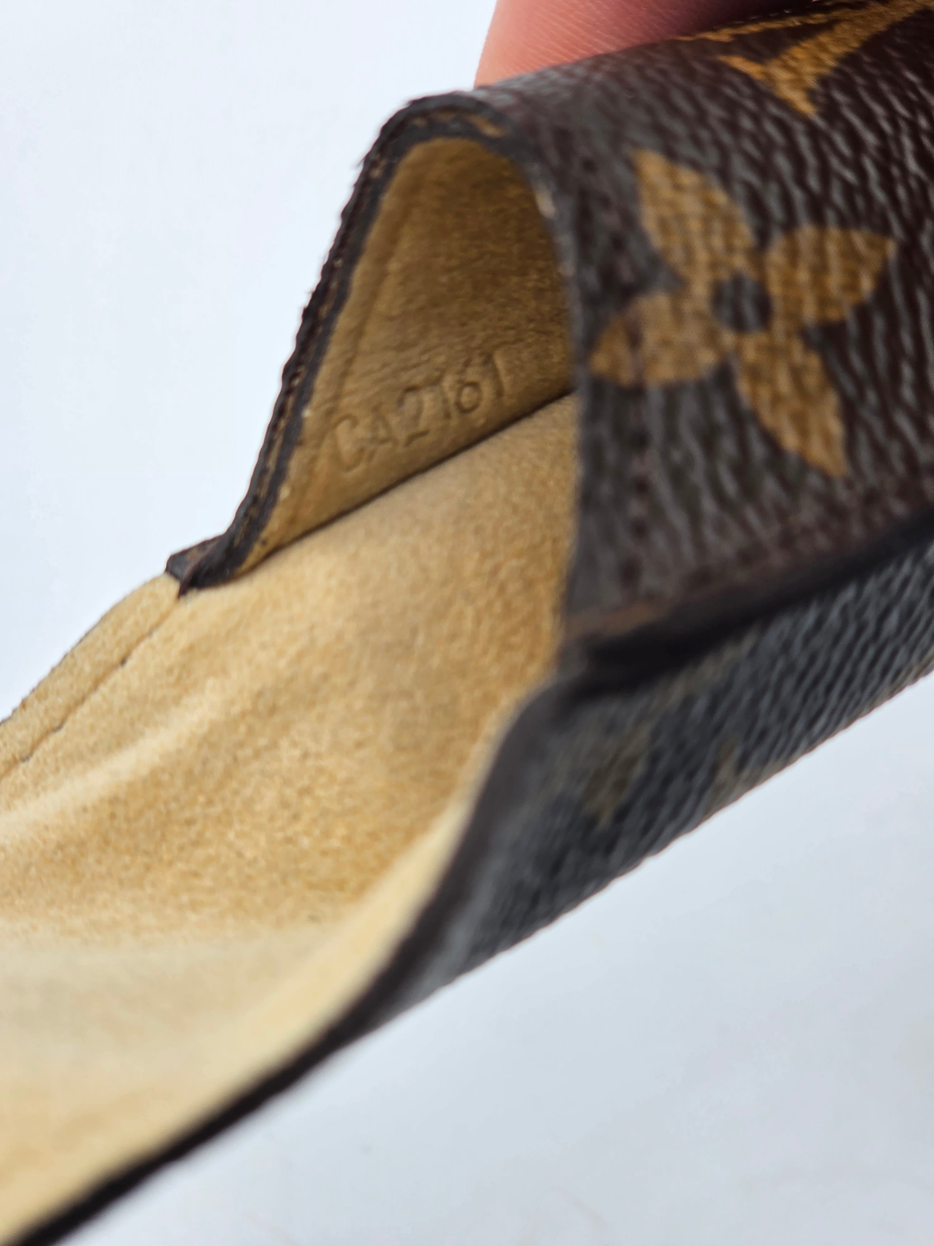 Close-up of a Louis Vuitton monogram leather item, showing the dark brown coated canvas with tan floral pattern and a beige suede interior.