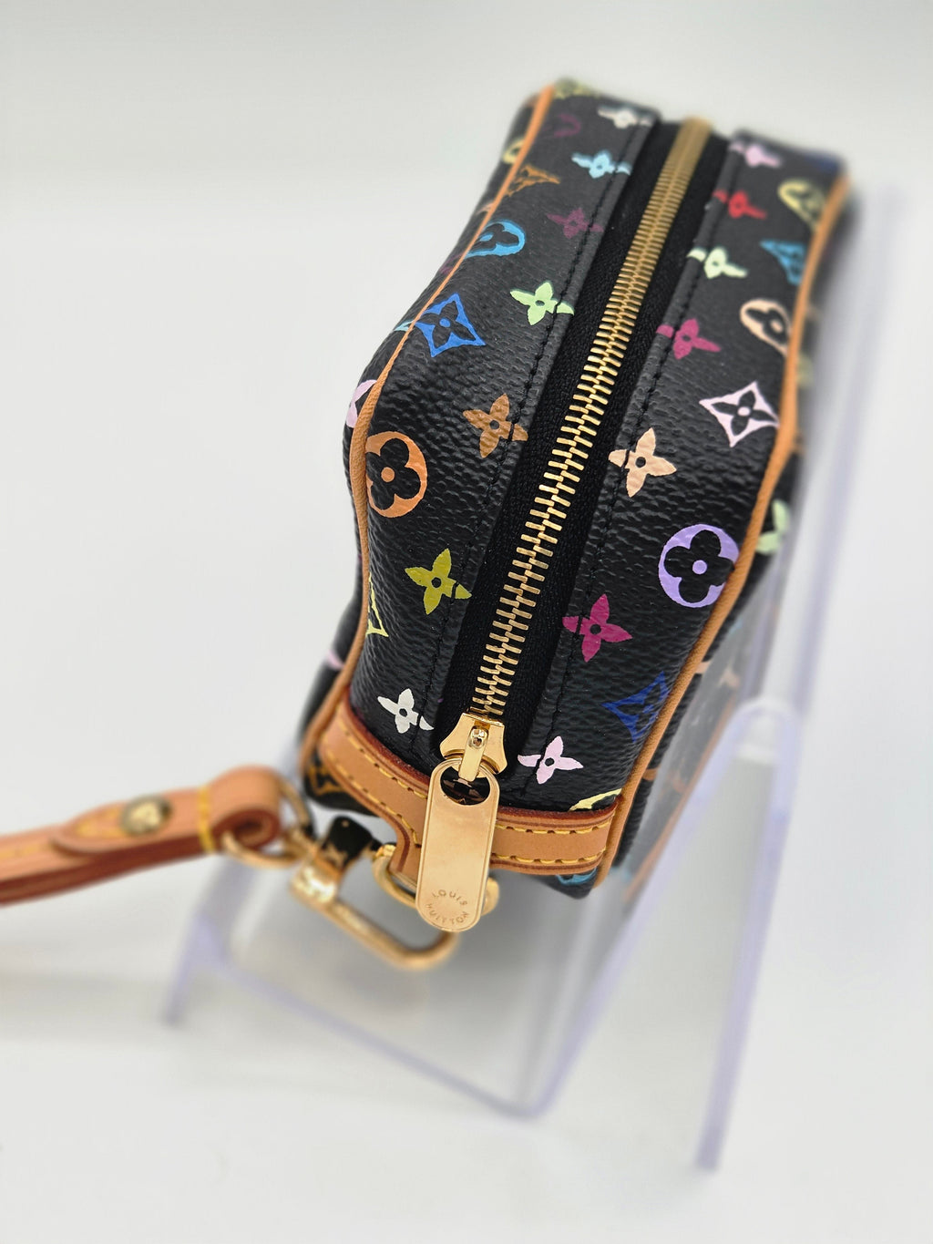A Louis Vuitton monogram canvas wristlet pouch with a colorful floral print on a black background, featuring gold-tone hardware and tan leather trim, shown on a white background.