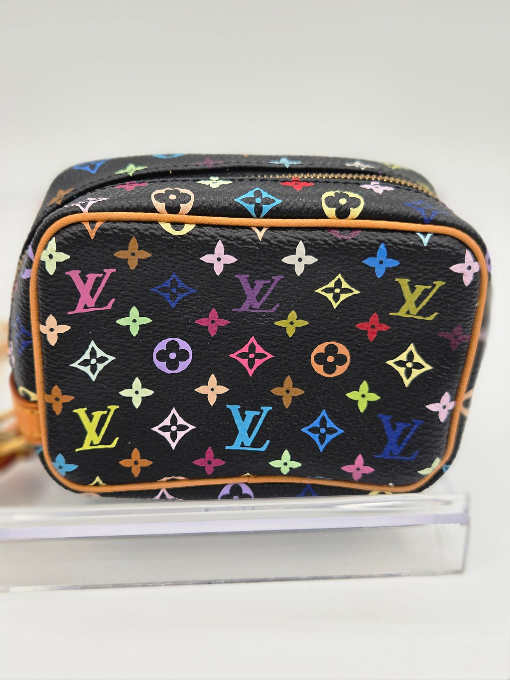 A Louis Vuitton toiletry bag in black multicolor monogram canvas, displayed on a clear acrylic stand against a white background.