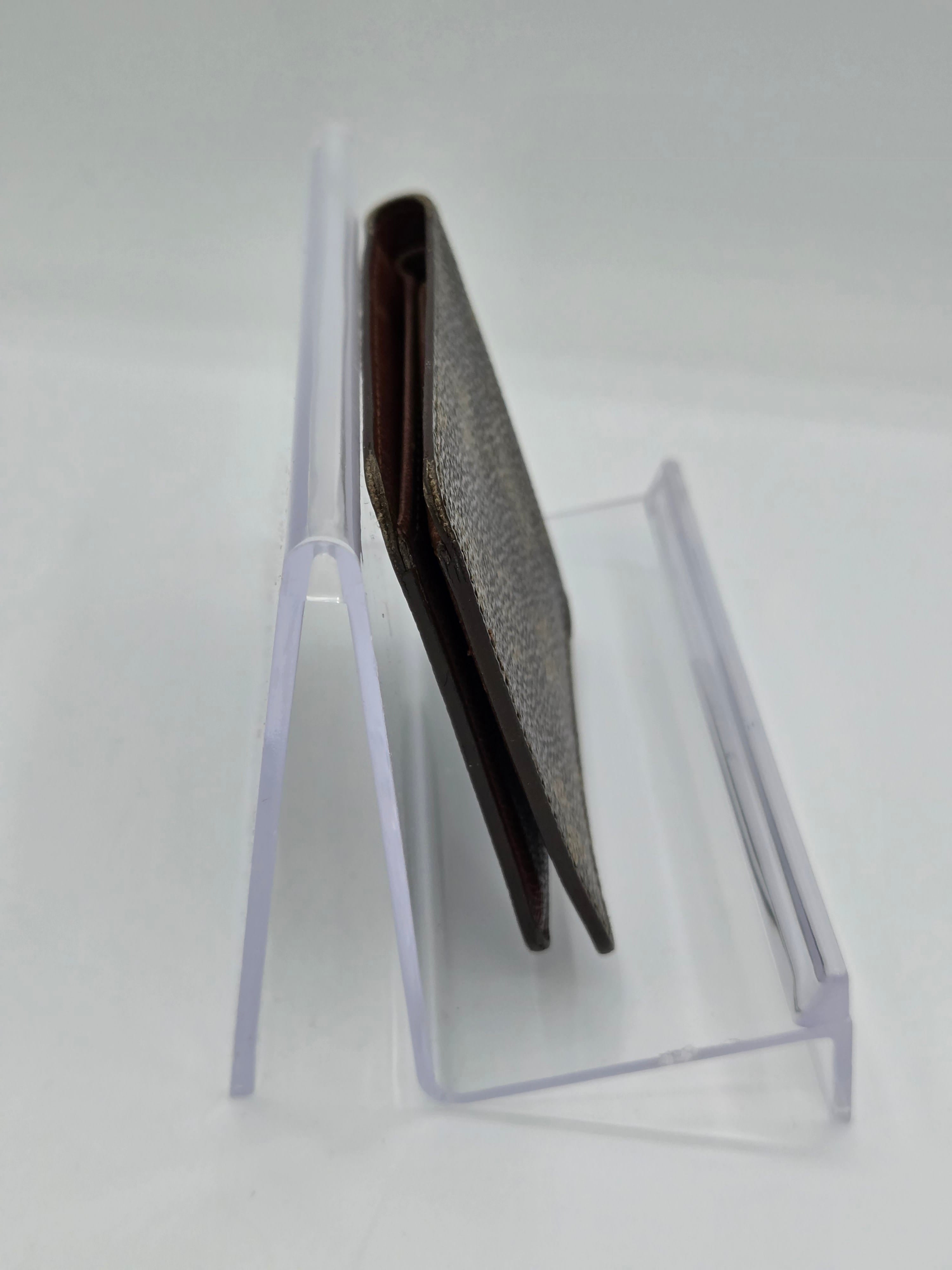 A dark brown textured leather wallet or card holder resting inside a clear acrylic display stand against a plain white background.