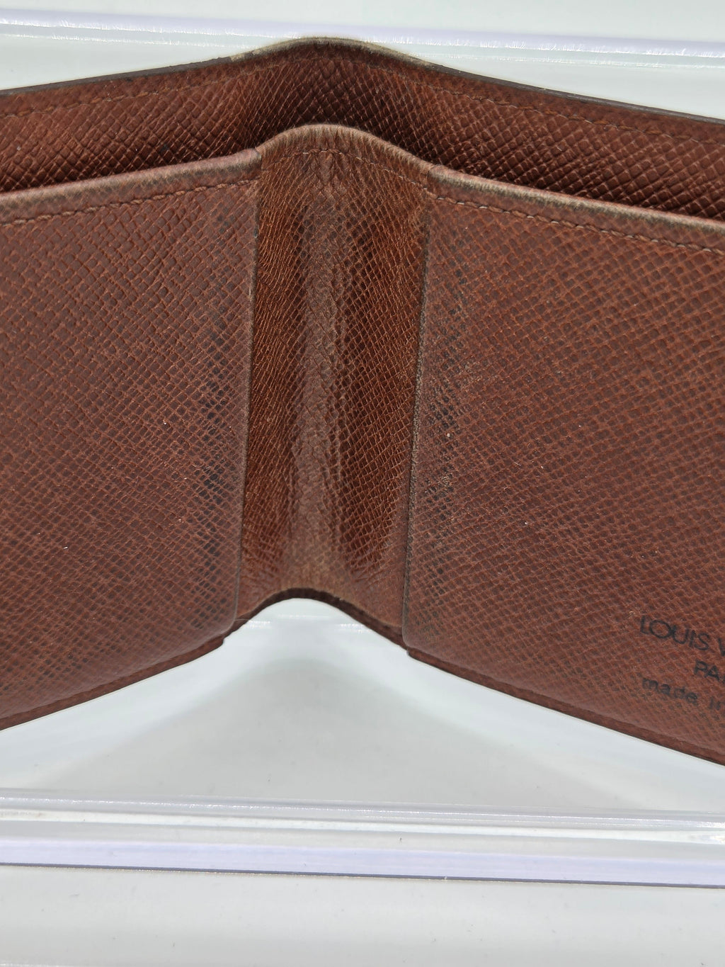A close-up of an open brown textured leather wallet, showing the interior lining and card slots, with a small embossed Louis Vuitton logo visible on the right side.