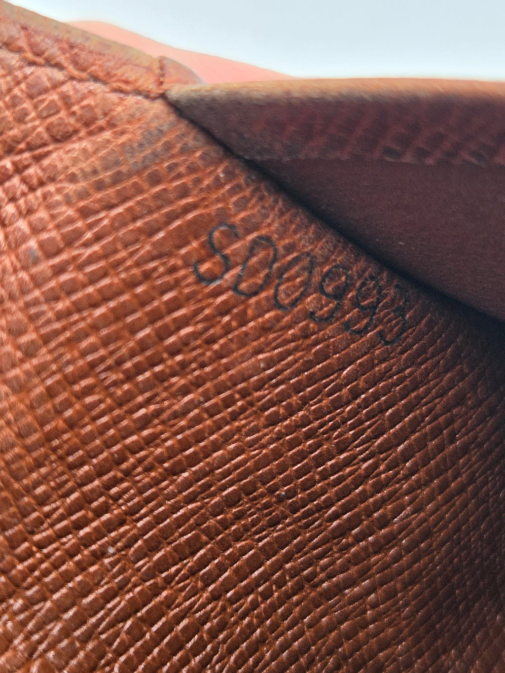 Close-up of a brown textured leather surface with embossed black numbering and a folded corner showing a darker brown interior.
