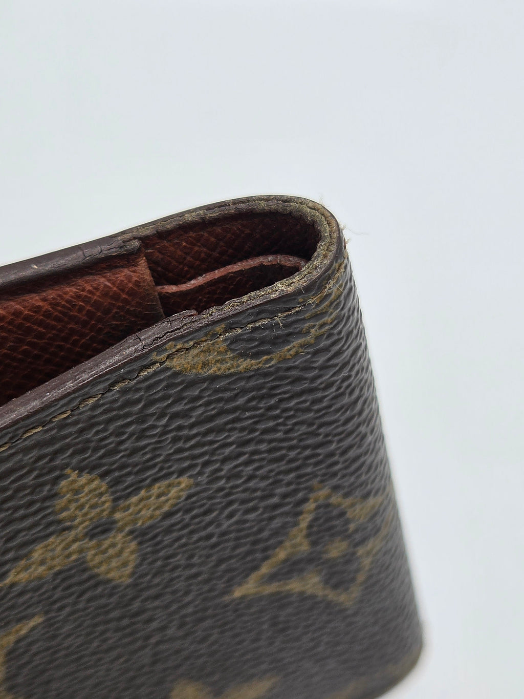 Close-up of a brown monogram wallet or clutch showing the textured canvas exterior and interior lining against a plain light background.