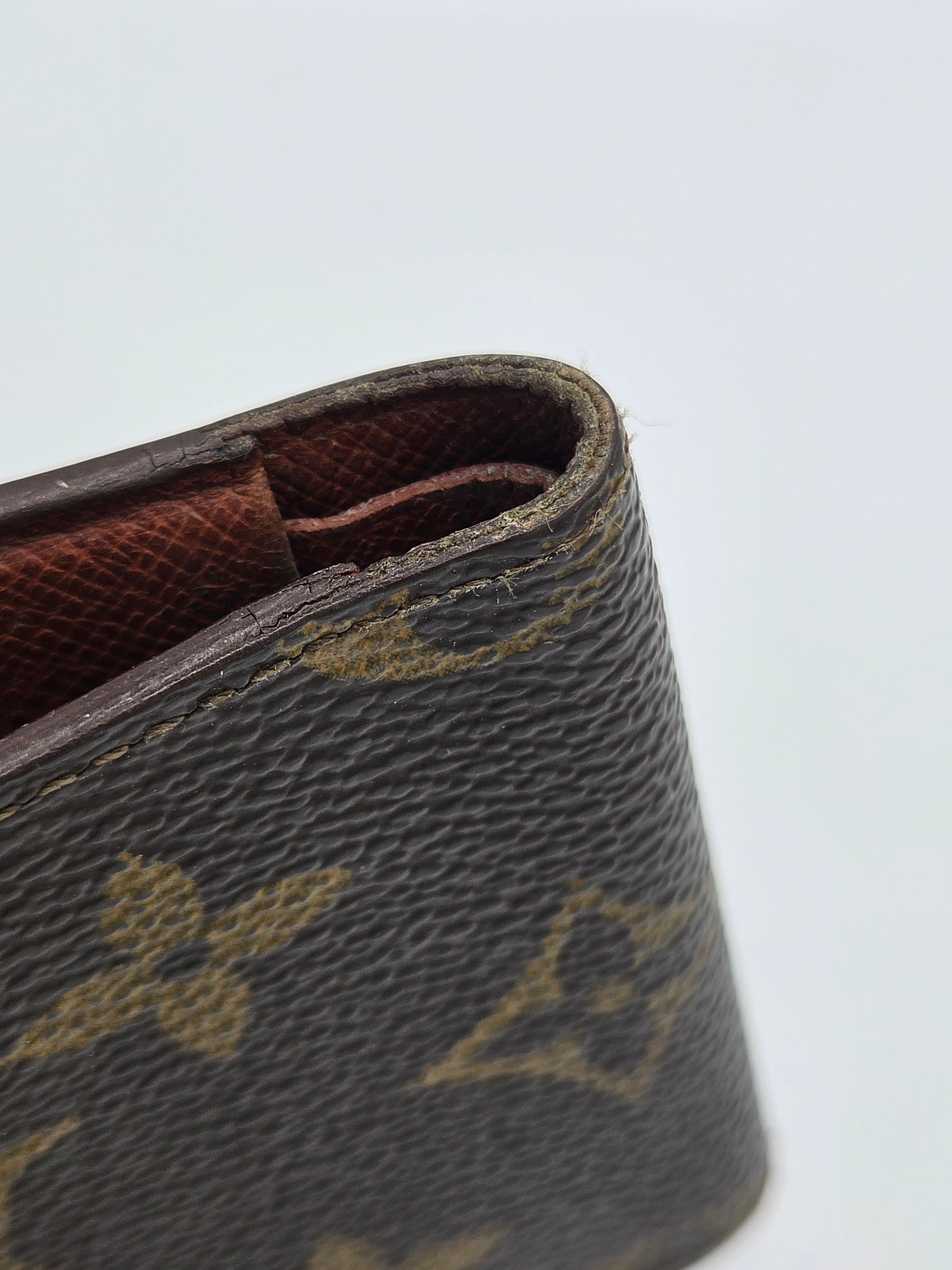 Close-up of a brown monogram wallet or clutch showing the textured canvas exterior and interior lining against a plain light background.