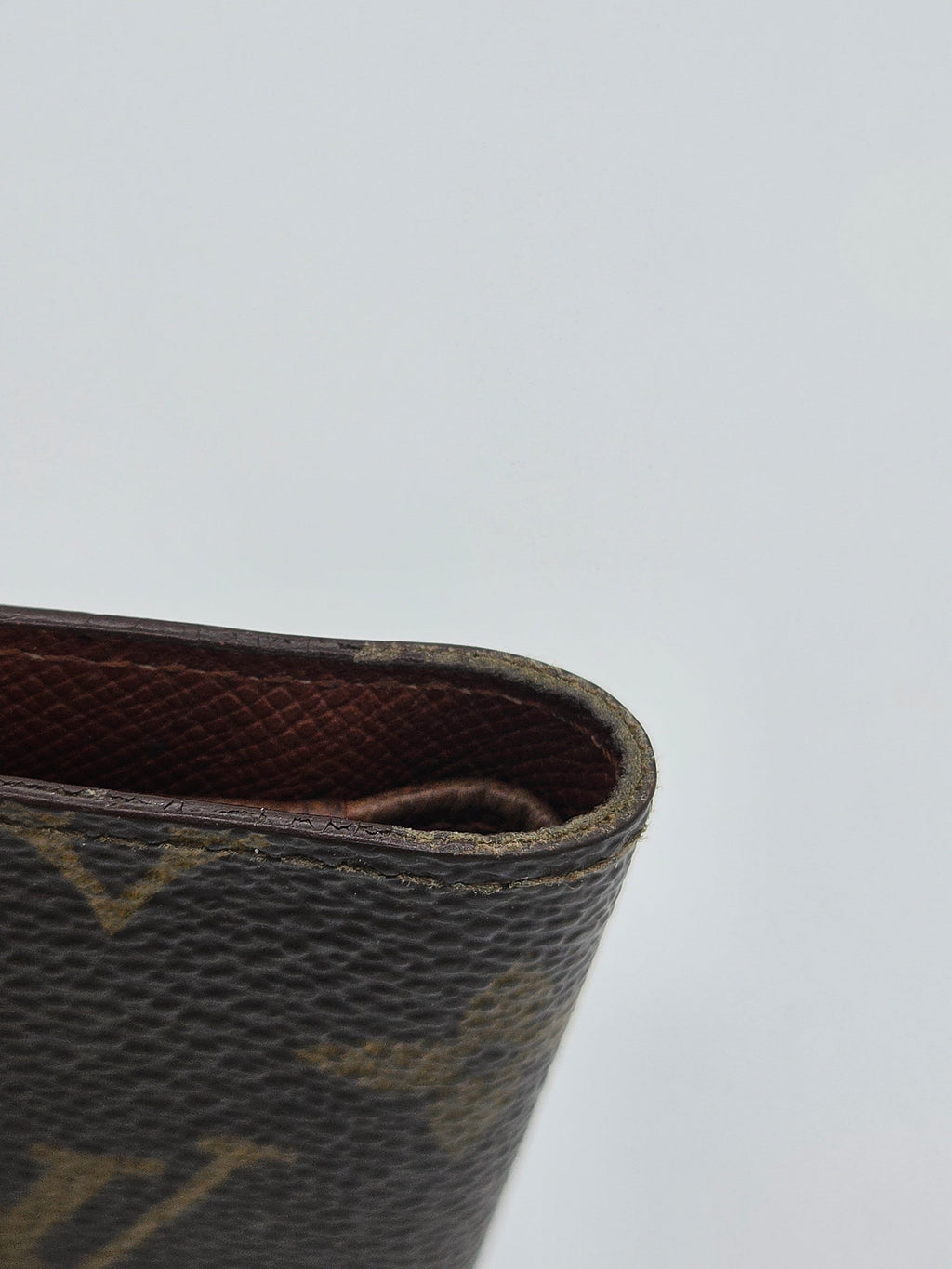 Close-up of a dark brown monogram canvas wallet corner showing the textured canvas pattern and interior lining against a light gray background.