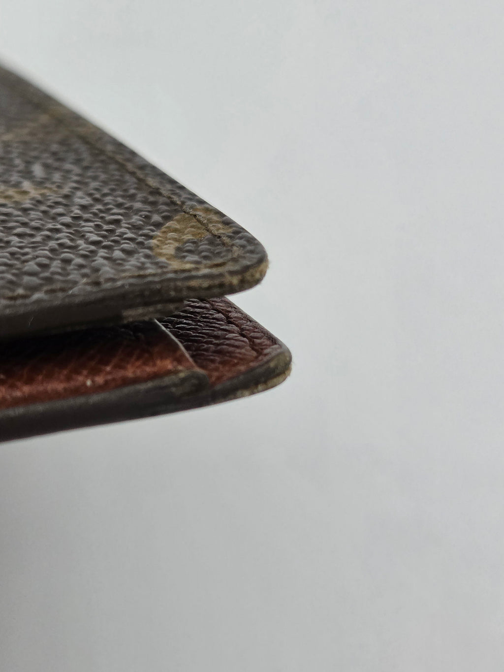 Close-up of the corner of a dark brown textured leather item, showing the edge and interior lining against a plain light gray background.