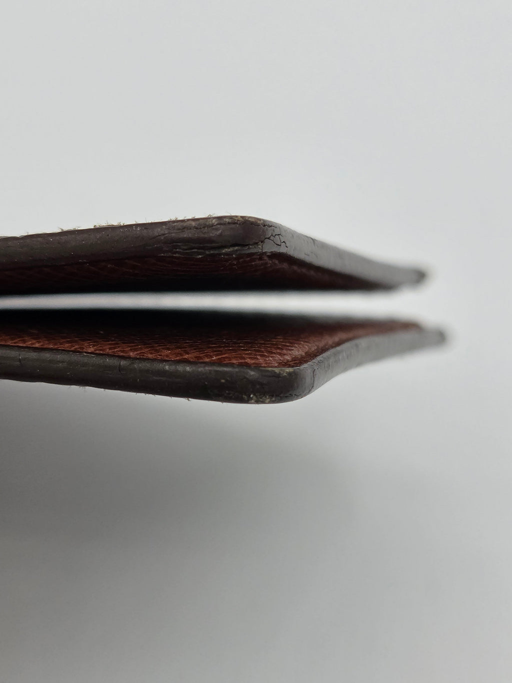 Close-up of the side profile of a dark brown leather wallet or card holder, showing the textured leather edge against a light gray background.