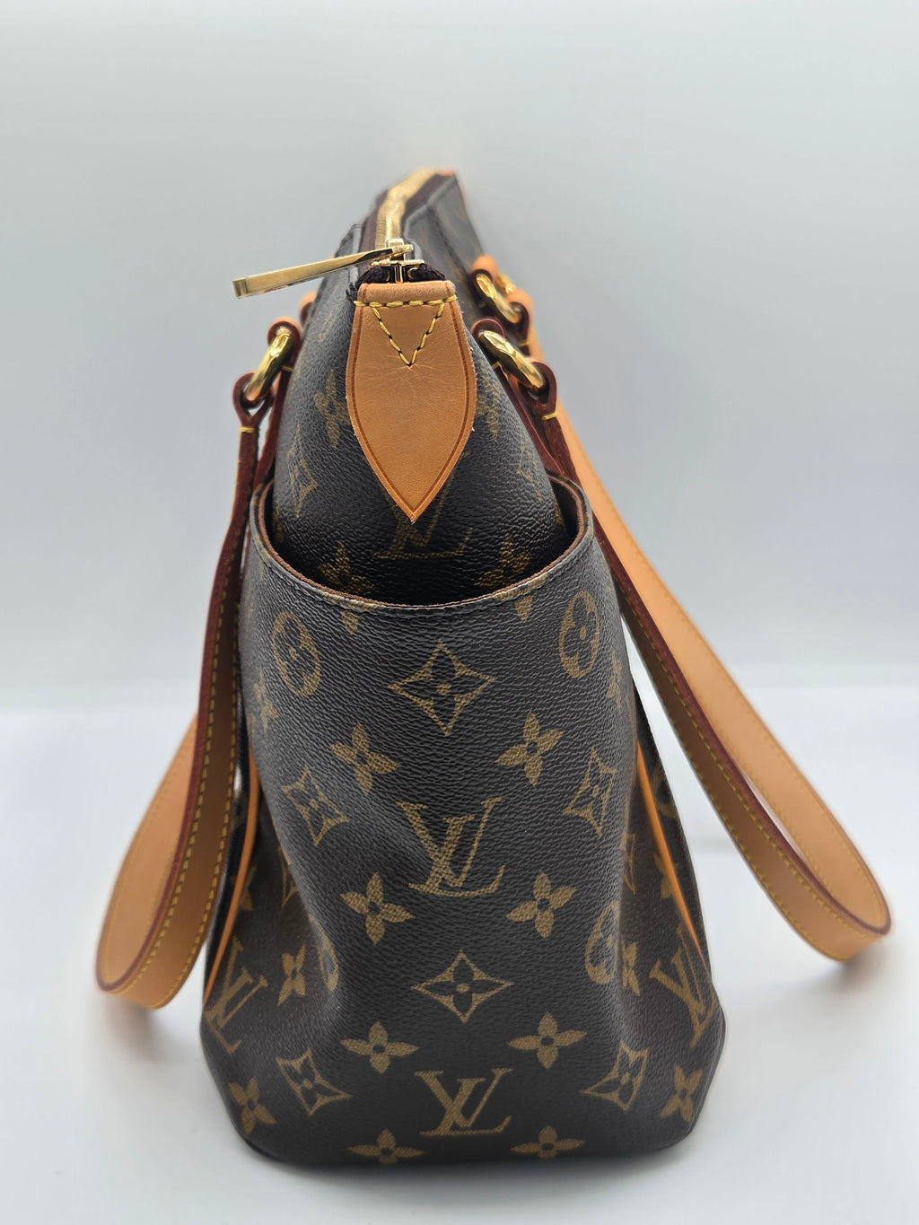 Louis Vuitton monogram canvas shoulder bag in dark brown with tan leather trim and gold-tone hardware, photographed against a light gray studio background.