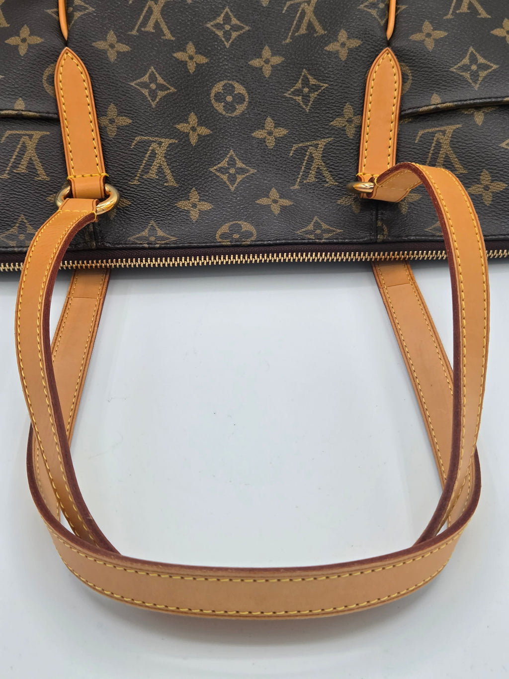 Close-up of a Louis Vuitton handbag in dark brown monogram canvas with tan leather handles and trim, shown against a plain white background.