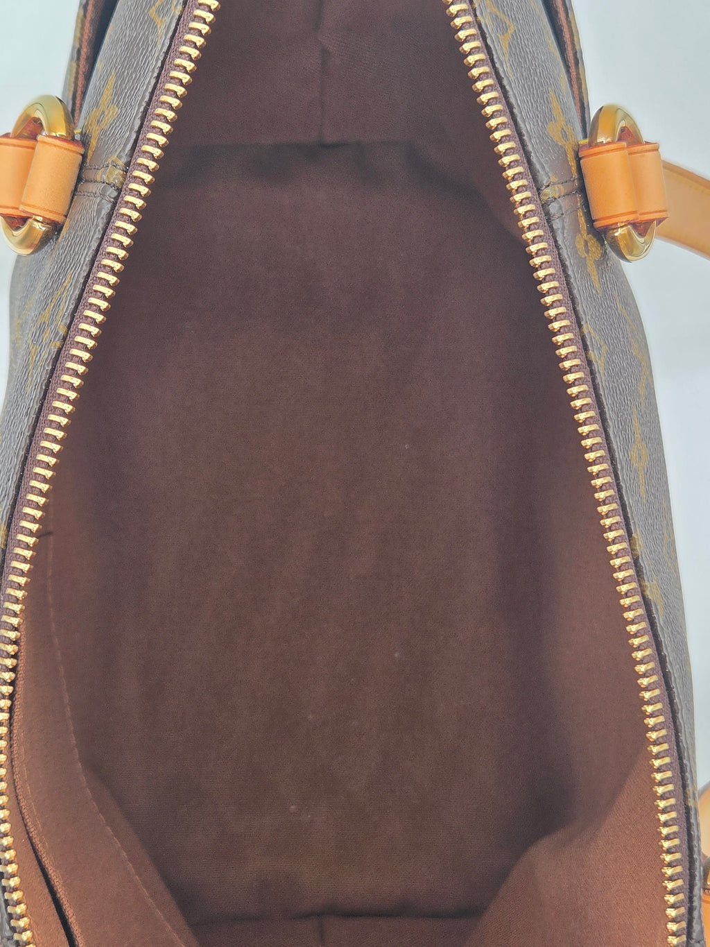 Close-up view of the interior of a Louis Vuitton handbag in brown monogram canvas, showing the dark brown suede-like lining and gold-tone zipper.