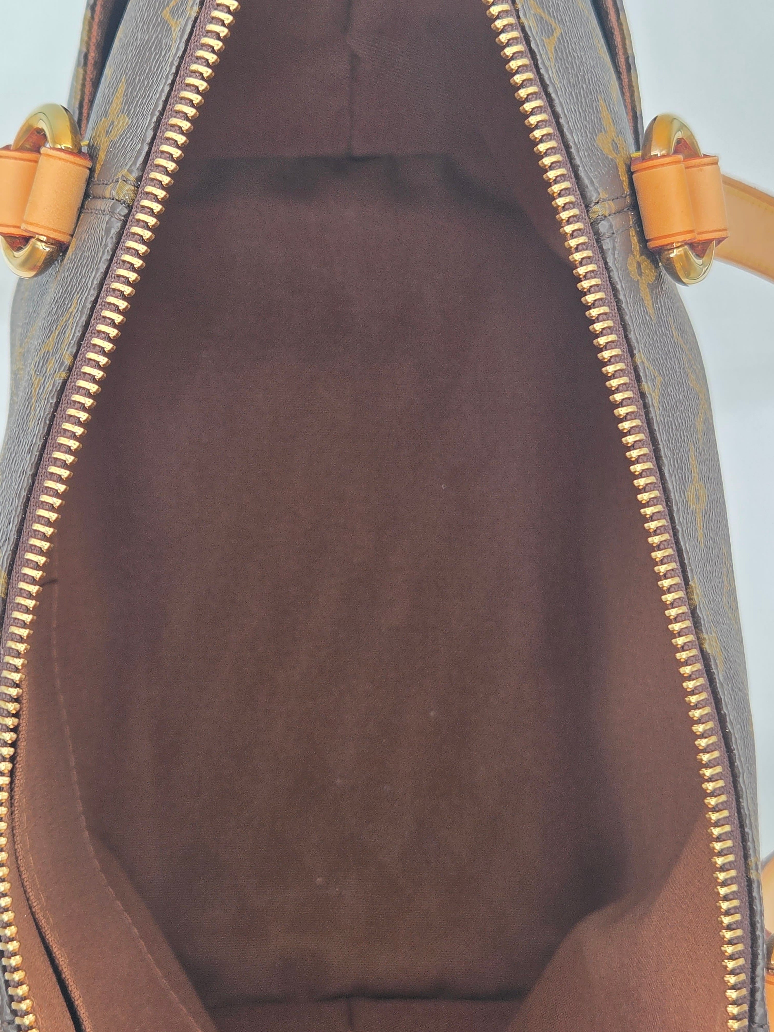 Close-up view of the interior of a Louis Vuitton handbag in brown monogram canvas, showing the dark brown suede-like lining and gold-tone zipper.