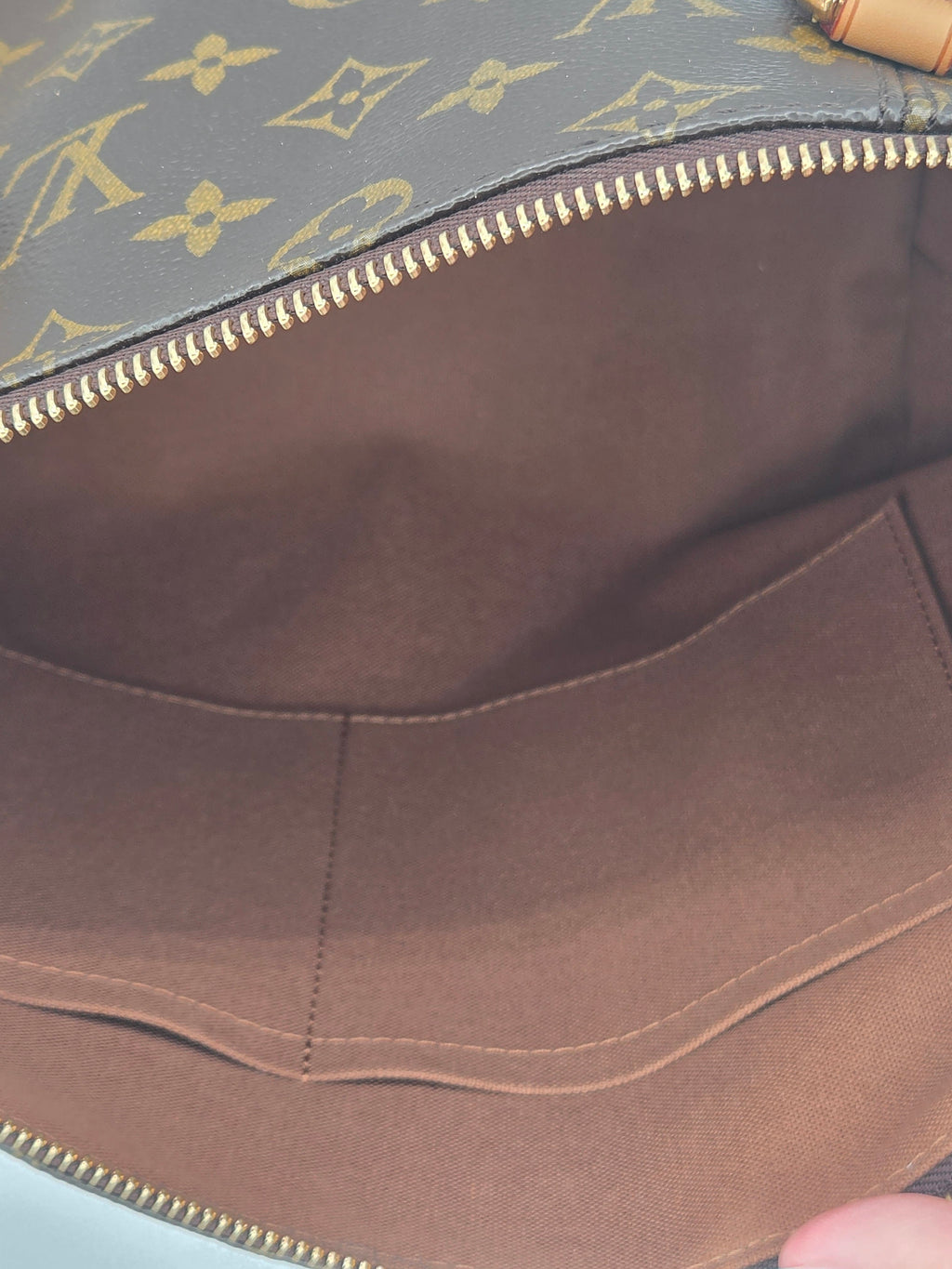 Close-up of the interior of a Louis Vuitton bag, showing the brown fabric lining, gold-tone zipper, and a portion of the gray monogram canvas on the left.