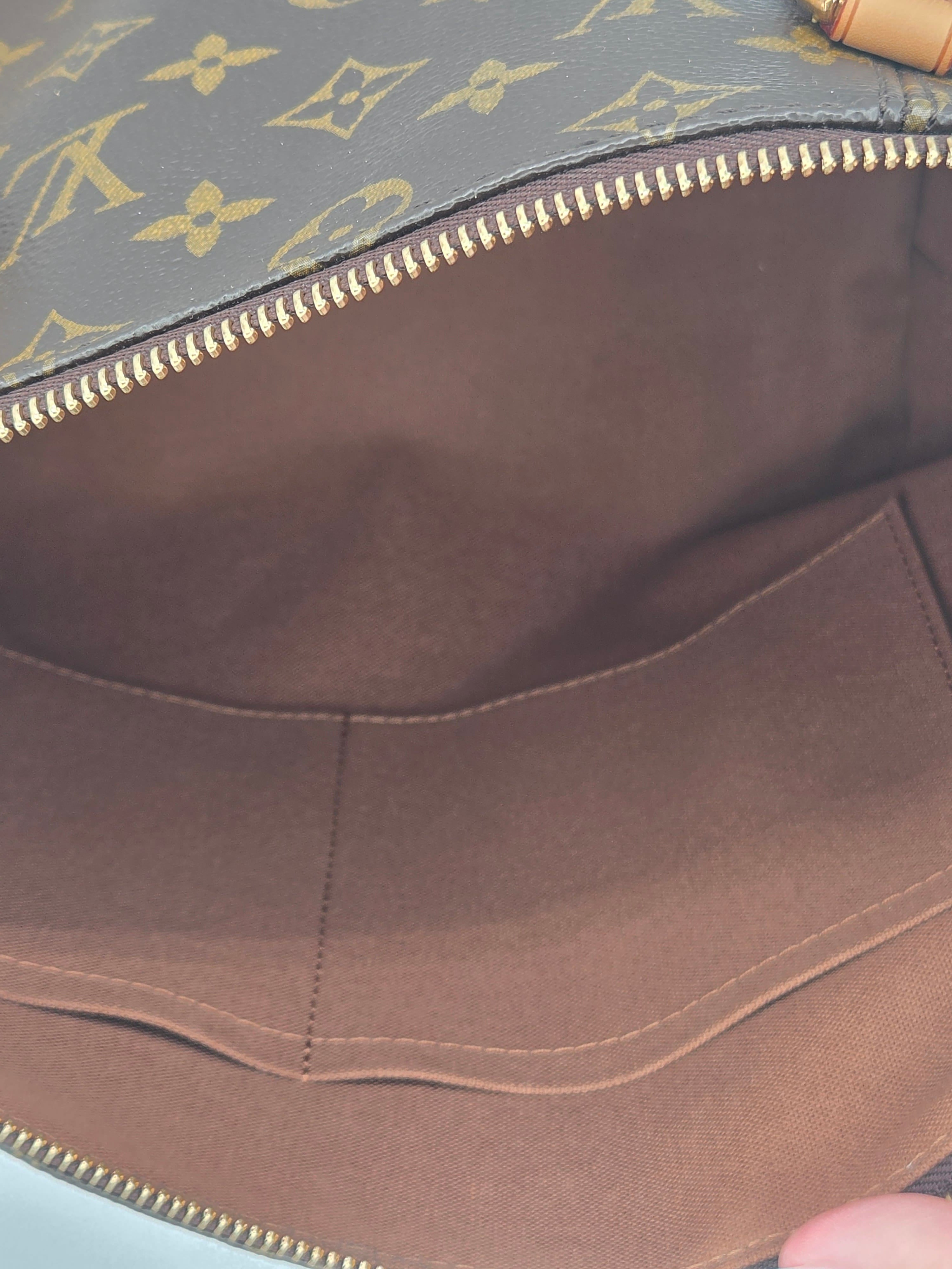Close-up of the interior of a Louis Vuitton bag, showing the brown fabric lining, gold-tone zipper, and a portion of the gray monogram canvas on the left.