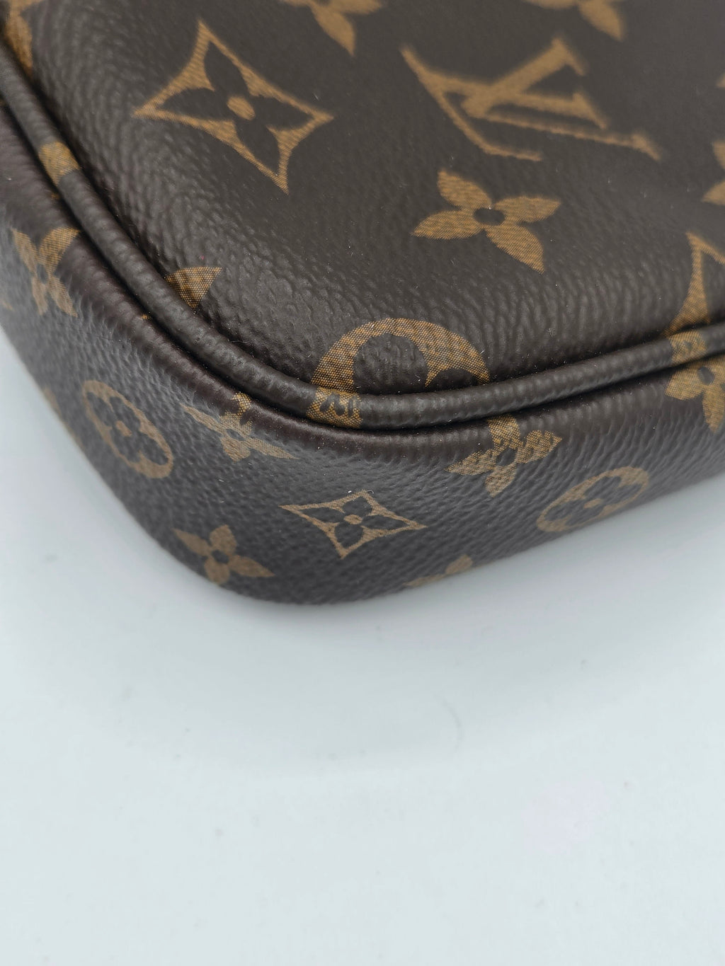 Close-up of a brown coated canvas item featuring the classic Louis Vuitton monogram pattern in tan, showing the corner and seam detail.