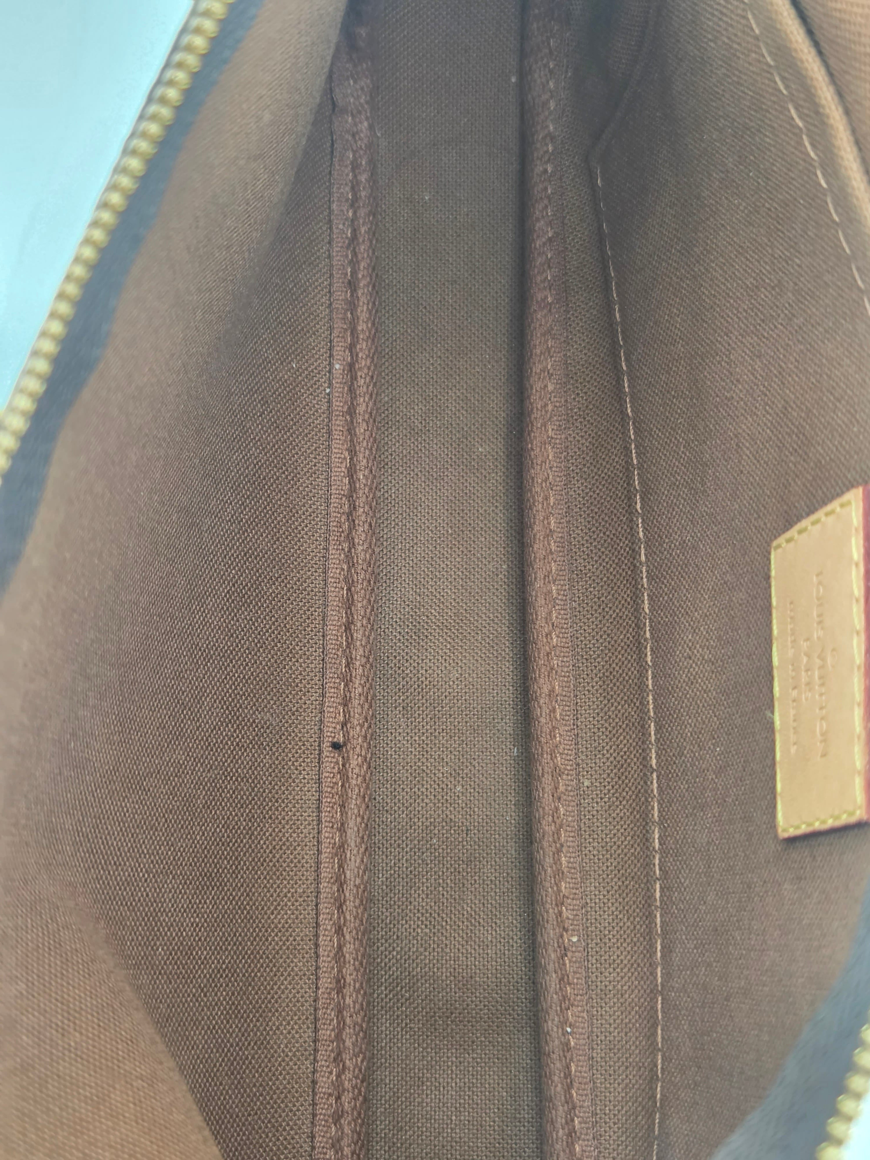 Close-up of the interior lining of a Louis Vuitton bag, showing a brown canvas body, double-stitched compartments, and a gold-tone zipper with a small beige brand patch at the top.