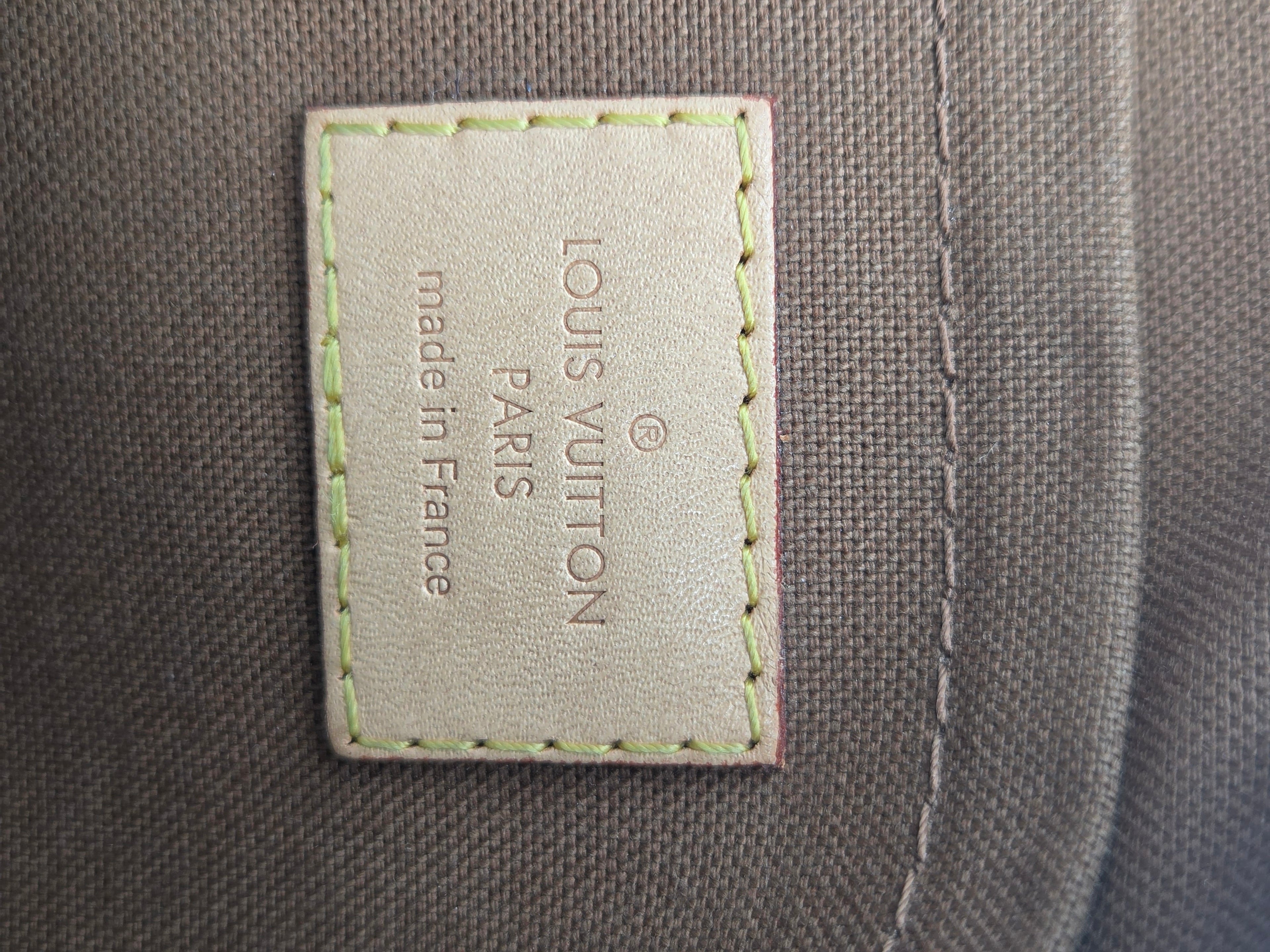 Close-up of a Louis Vuitton interior label sewn onto a gray canvas fabric, with light green stitching around the beige leather patch.