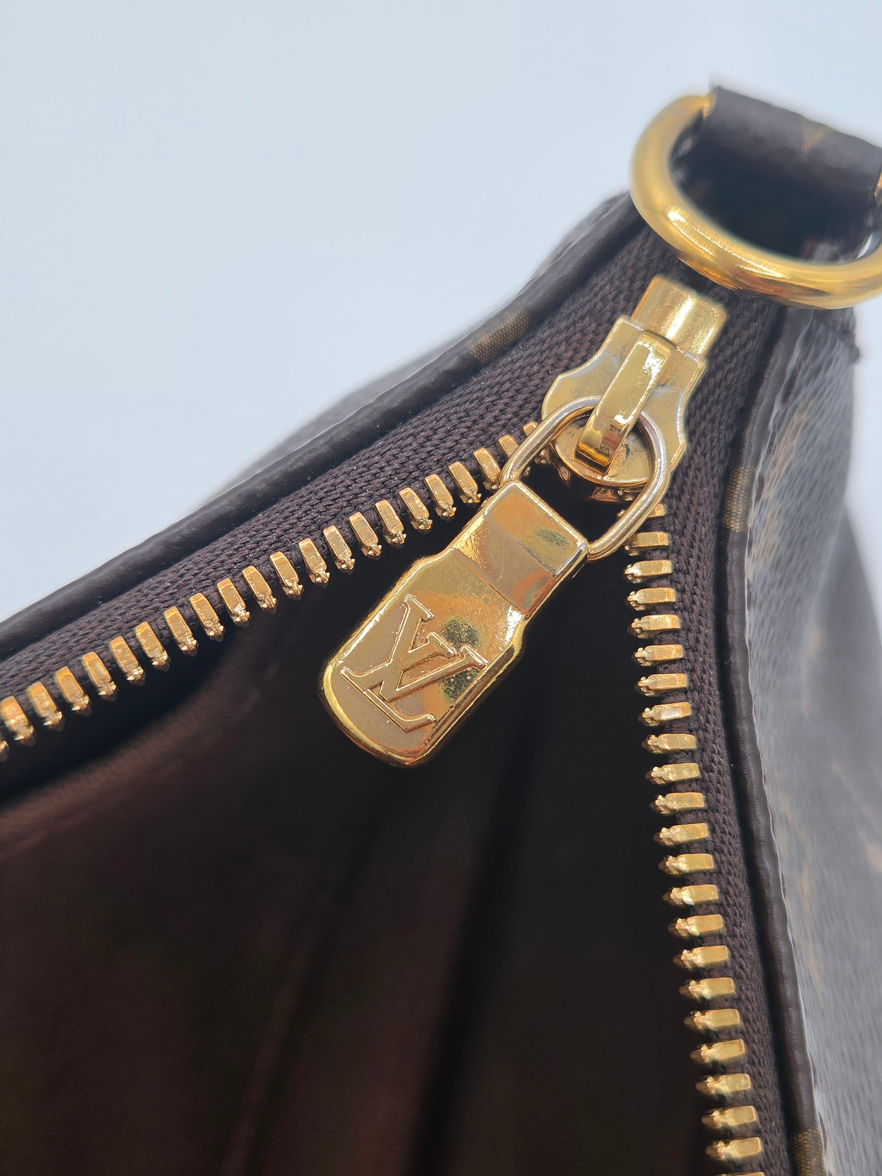 Close-up of a dark brown monogram canvas handbag with a gold-tone metal zipper pull featuring an embossed Louis Vuitton logo.