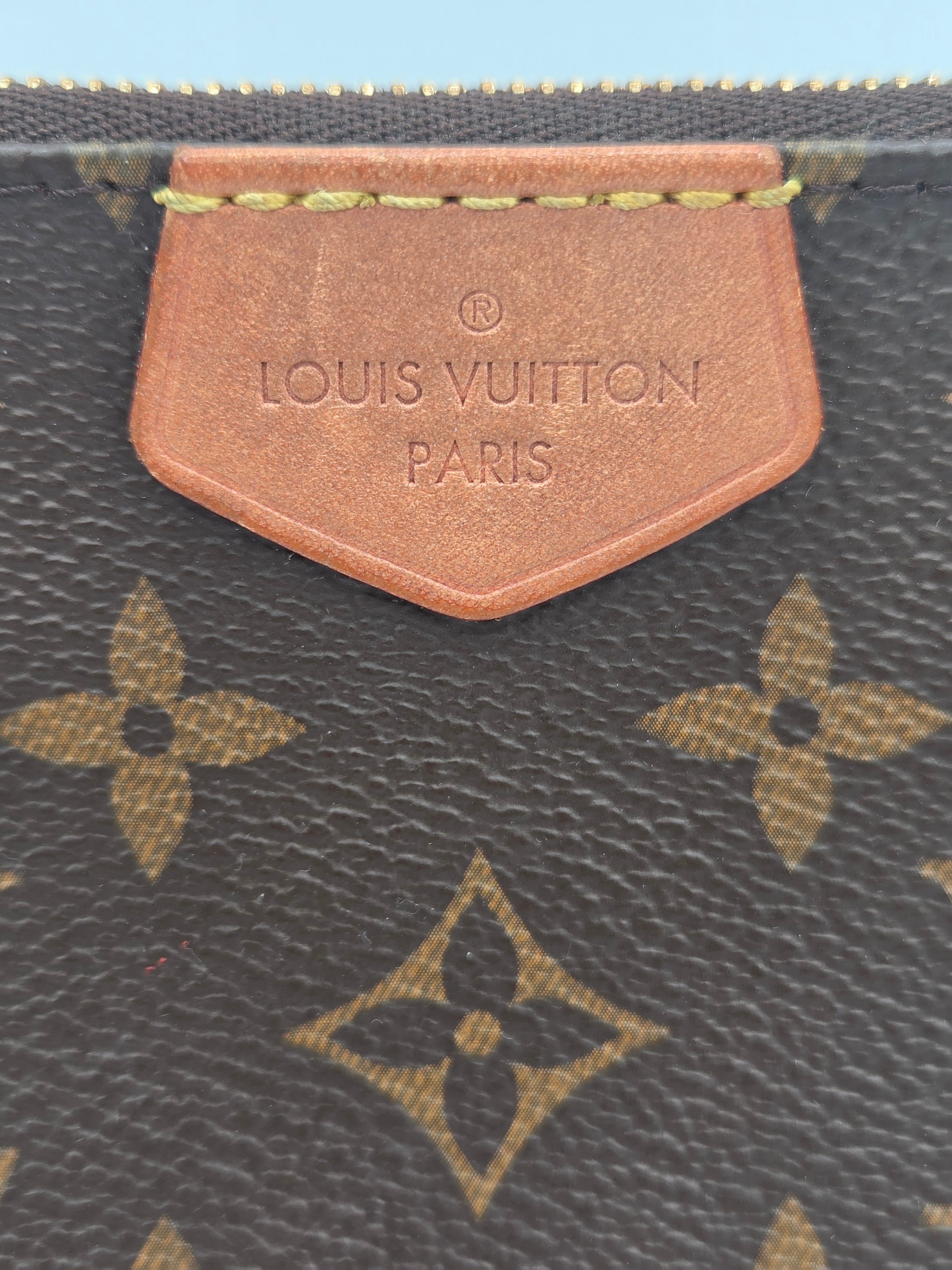 Close-up of a Louis Vuitton monogram coated canvas bag, showing the dark brown canvas with tan/gold monogram pattern and a tan leather brand tab embossed with 'LOUIS VUITTON PARIS'.