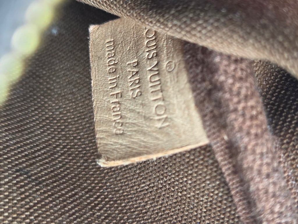 Close-up of a Louis Vuitton fabric tag sewn onto a dark brown woven canvas background.