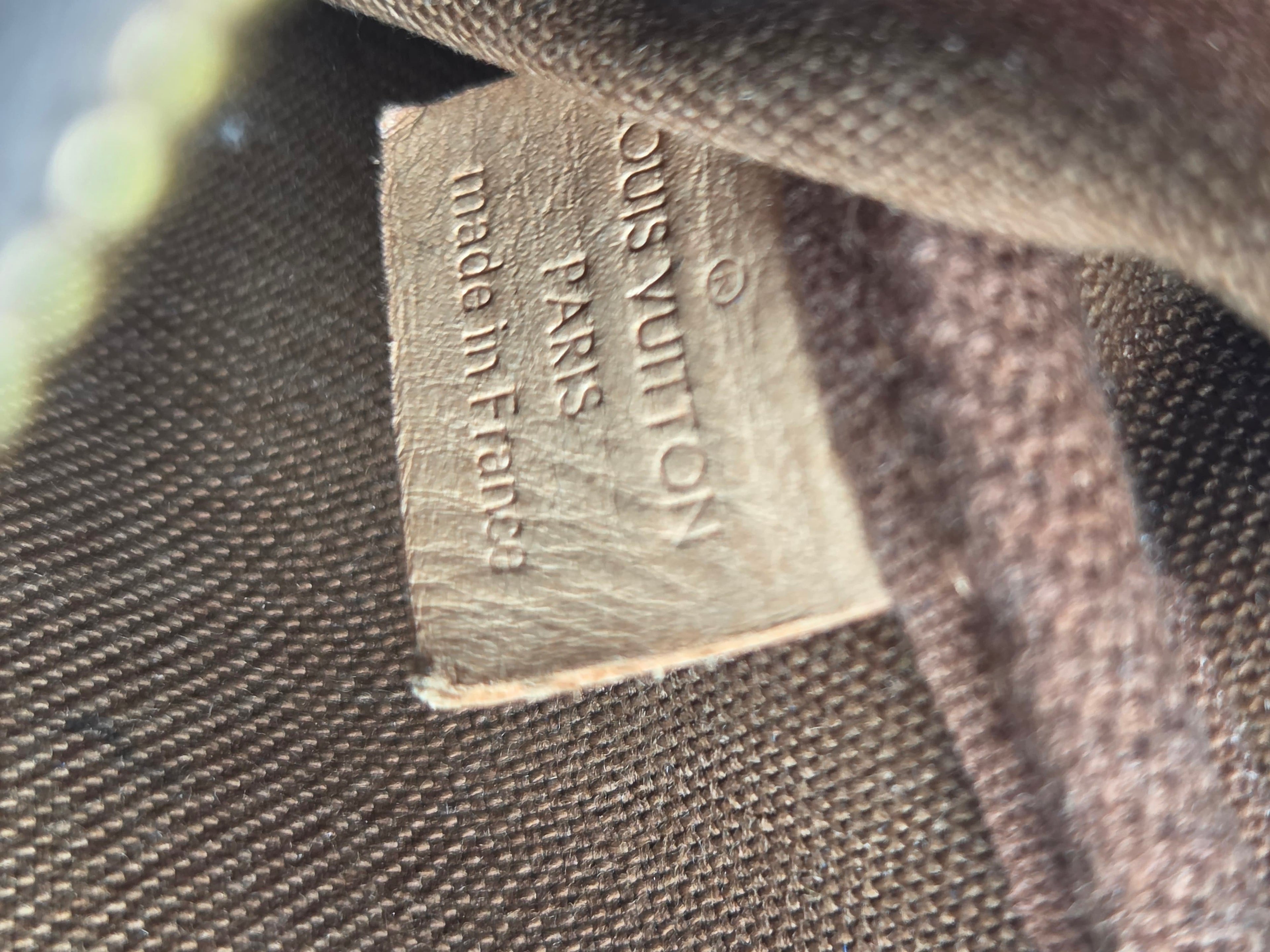 Close-up of a Louis Vuitton fabric tag sewn onto a dark brown woven canvas background.