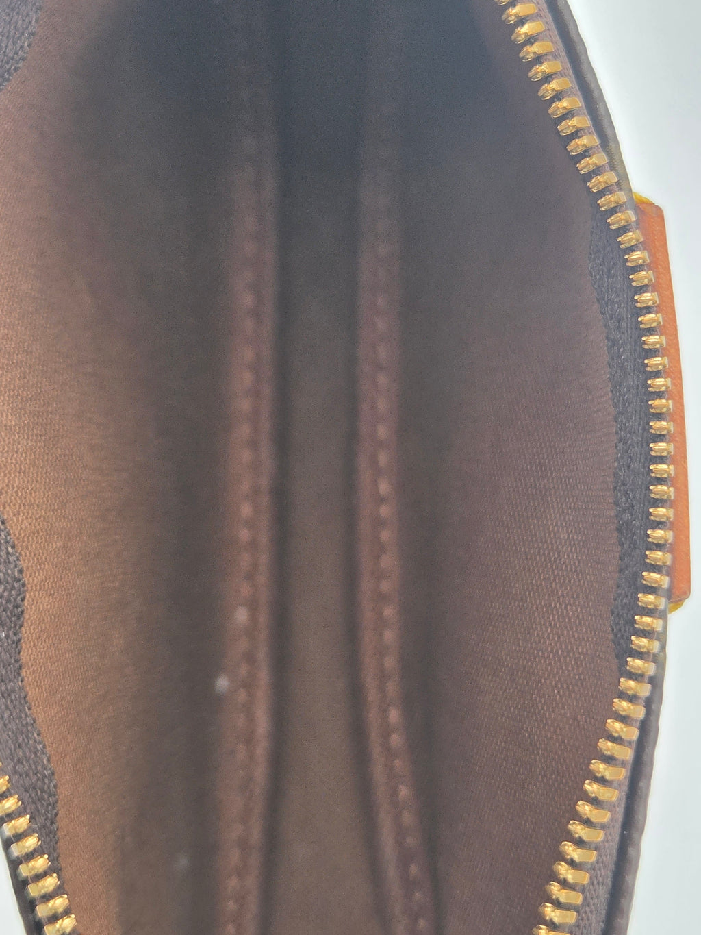 Close-up of the interior of a brown coated canvas zippered pouch, showing the brown fabric lining, gold zipper teeth, and a sliver of orange trim on the right side.