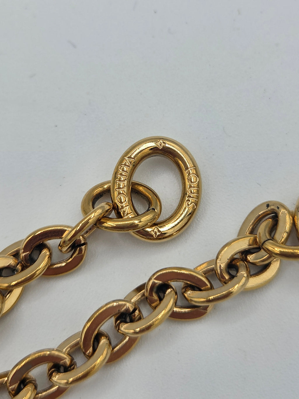Close-up of a gold-tone chain link necklace with a Louis Vuitton interlocking O-ring clasp, on a light gray background.