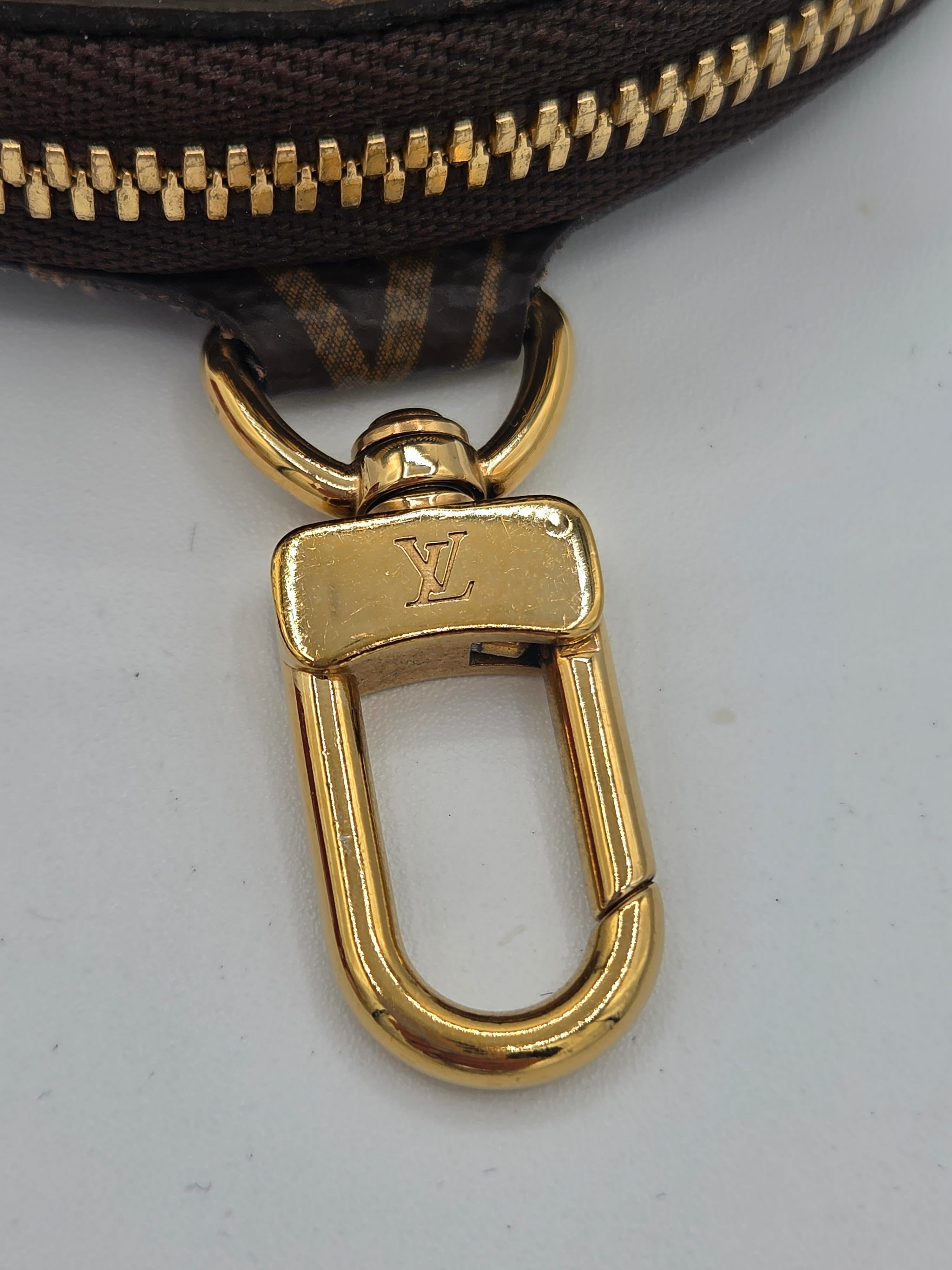 Close-up of a Louis Vuitton gold-tone metal swivel clasp attached to a dark brown monogram zipper pouch on a light gray background.