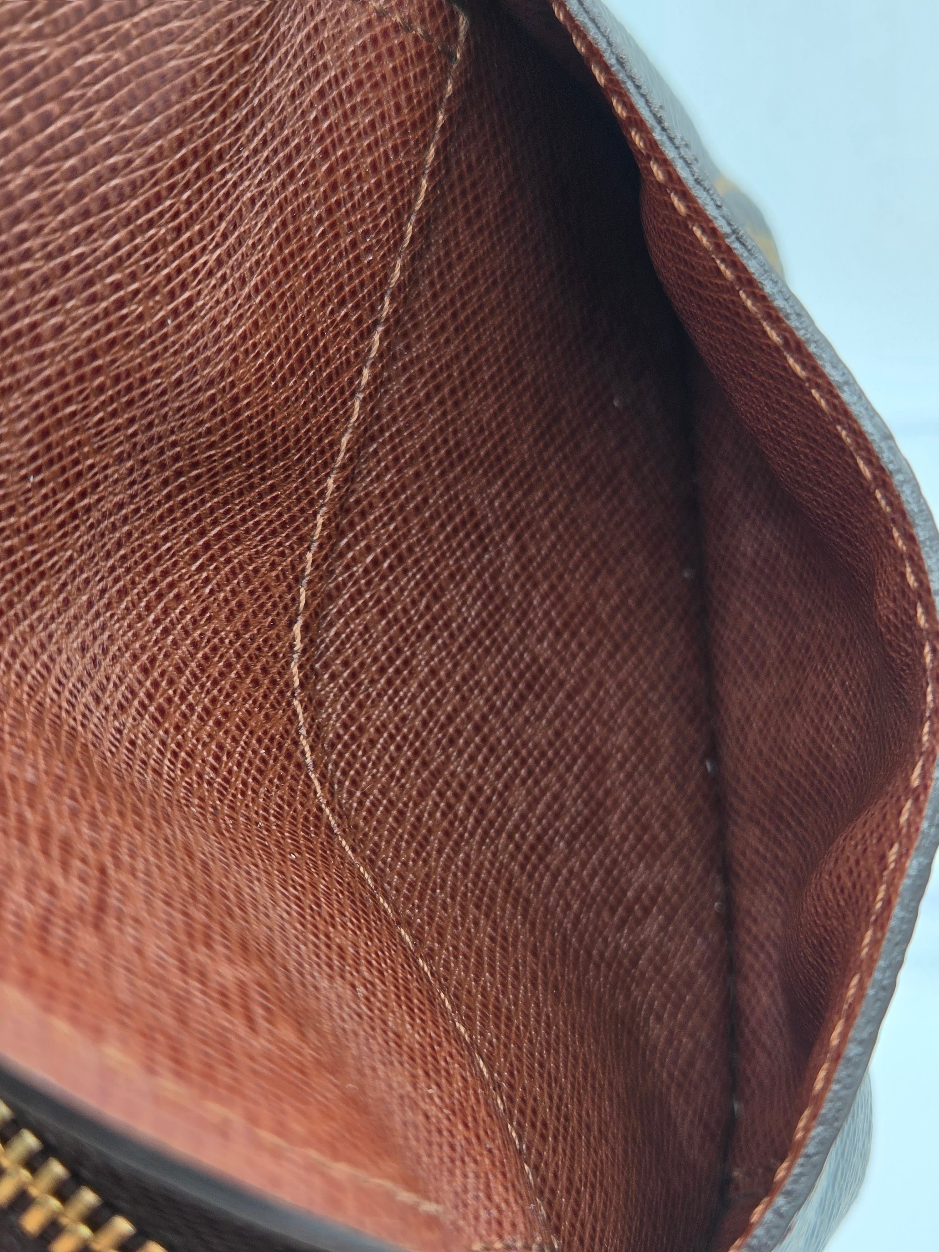 Close-up of the interior lining of a brown textured leather or faux-leather pouch, showing the stitched inner flap and zipper edge.