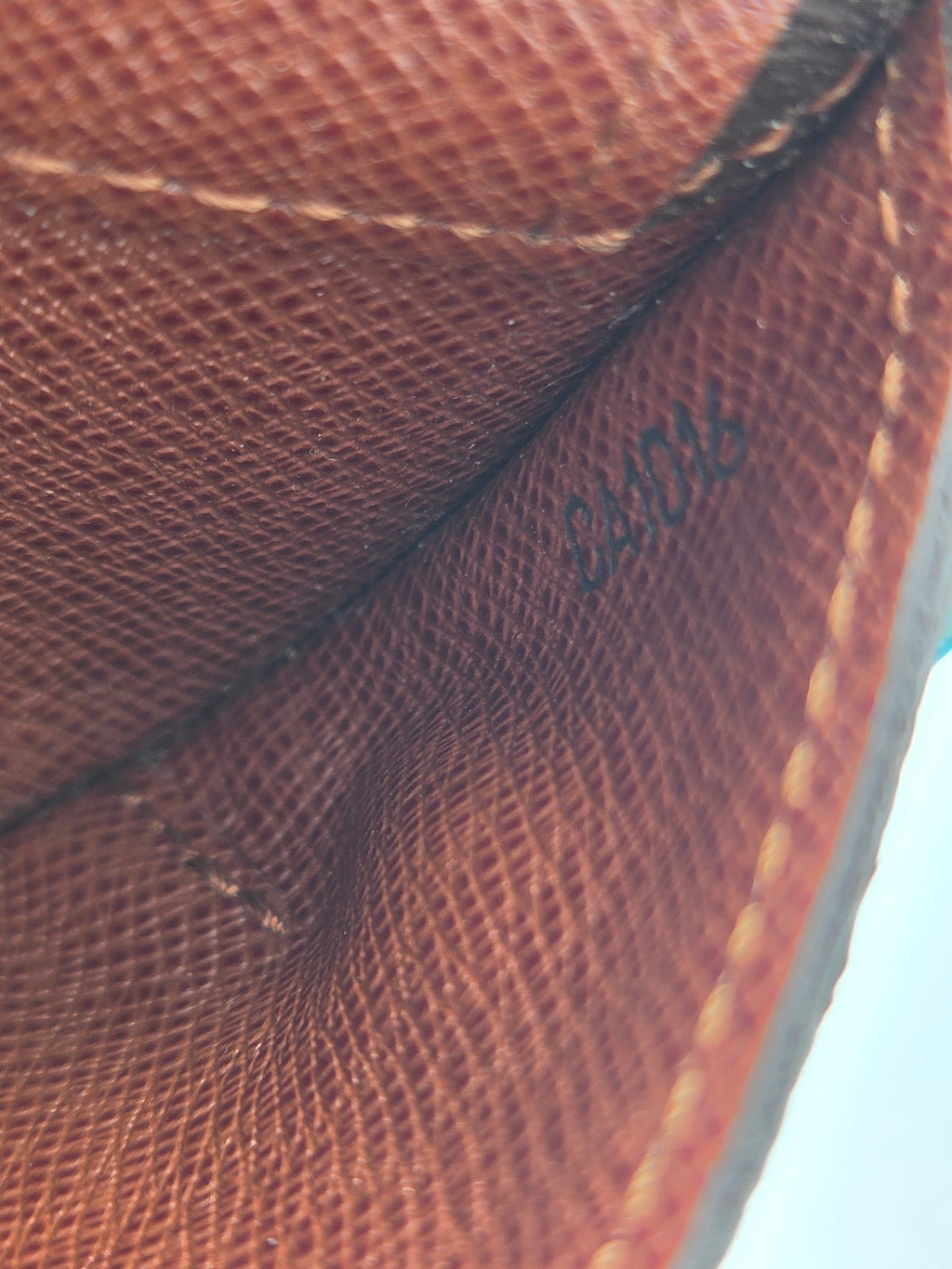 Close-up of a brown textured leather or canvas material with visible stitching and a faint embossed brand mark reading Louis Vuitton.