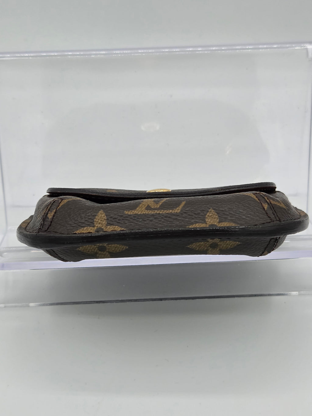 A Louis Vuitton monogram canvas pouch shown vertically inside a clear plastic display case against a white background.