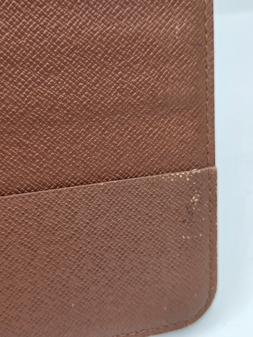 Close-up of a brown textured leather or faux-leather item, showing a fine grain pattern and a vertical seam with some dust or lint visible on the right side.