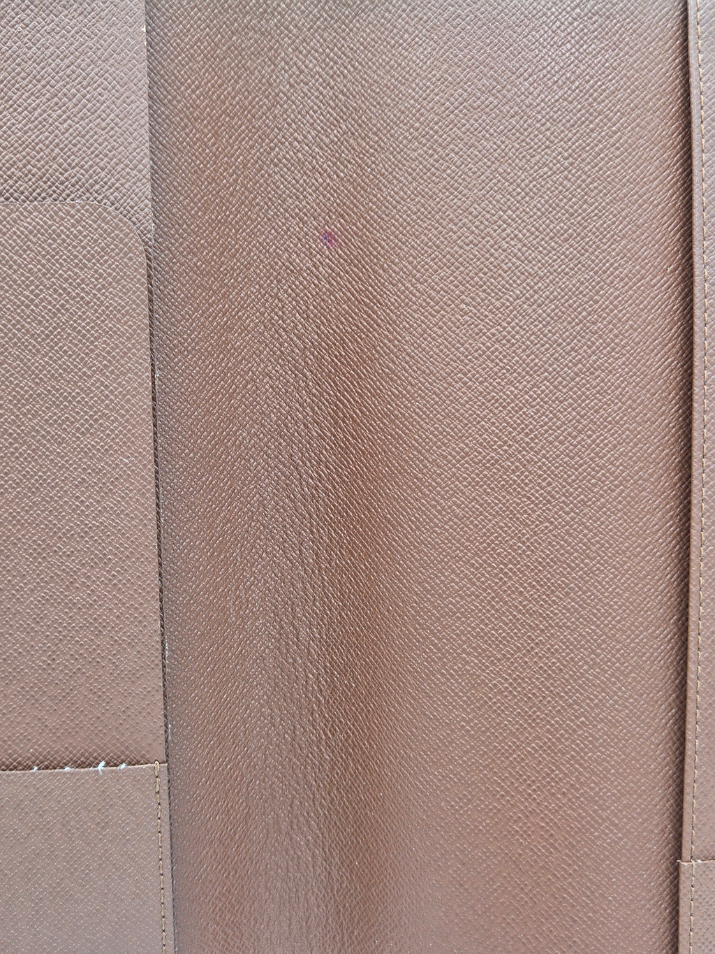 A close-up of a textured fabric or leather material in a warm taupe-beige color, showing a fine grain pattern and stitched panel seams.