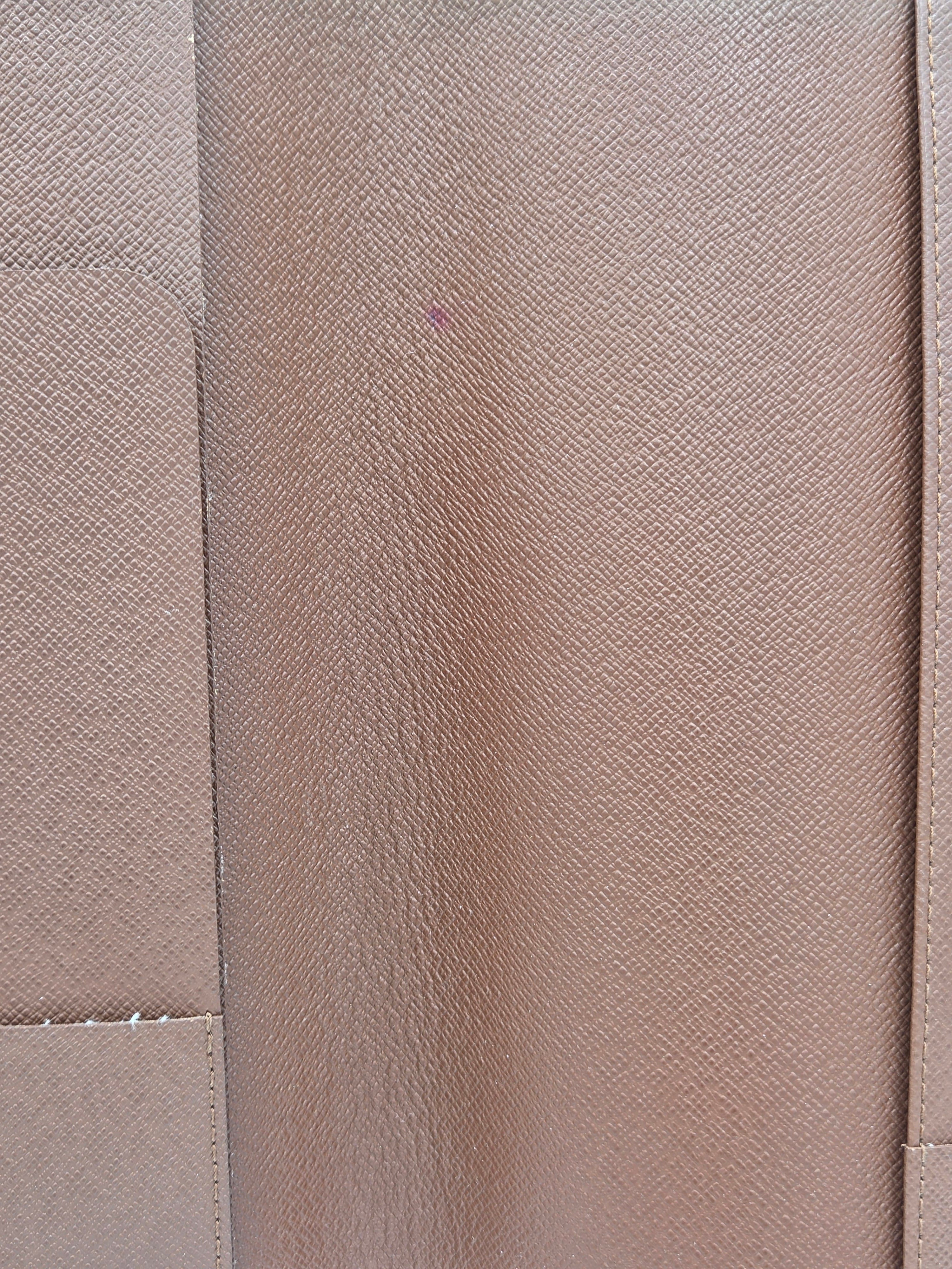 A close-up of a textured fabric or leather material in a warm taupe-beige color, showing a fine grain pattern and stitched panel seams.