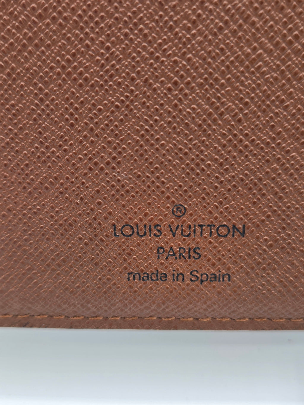 Close-up of a Louis Vuitton brown textured leather item, showing the embossed logo and 'made in Spain' text on a white background.