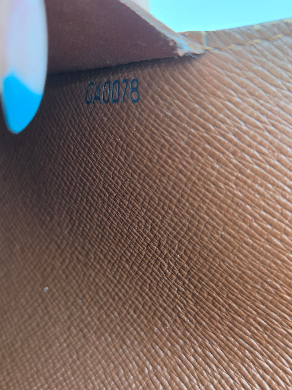 Close-up of a brown textured leather interior with embossed numbering and a small blue-tipped finger visible at the bottom left.