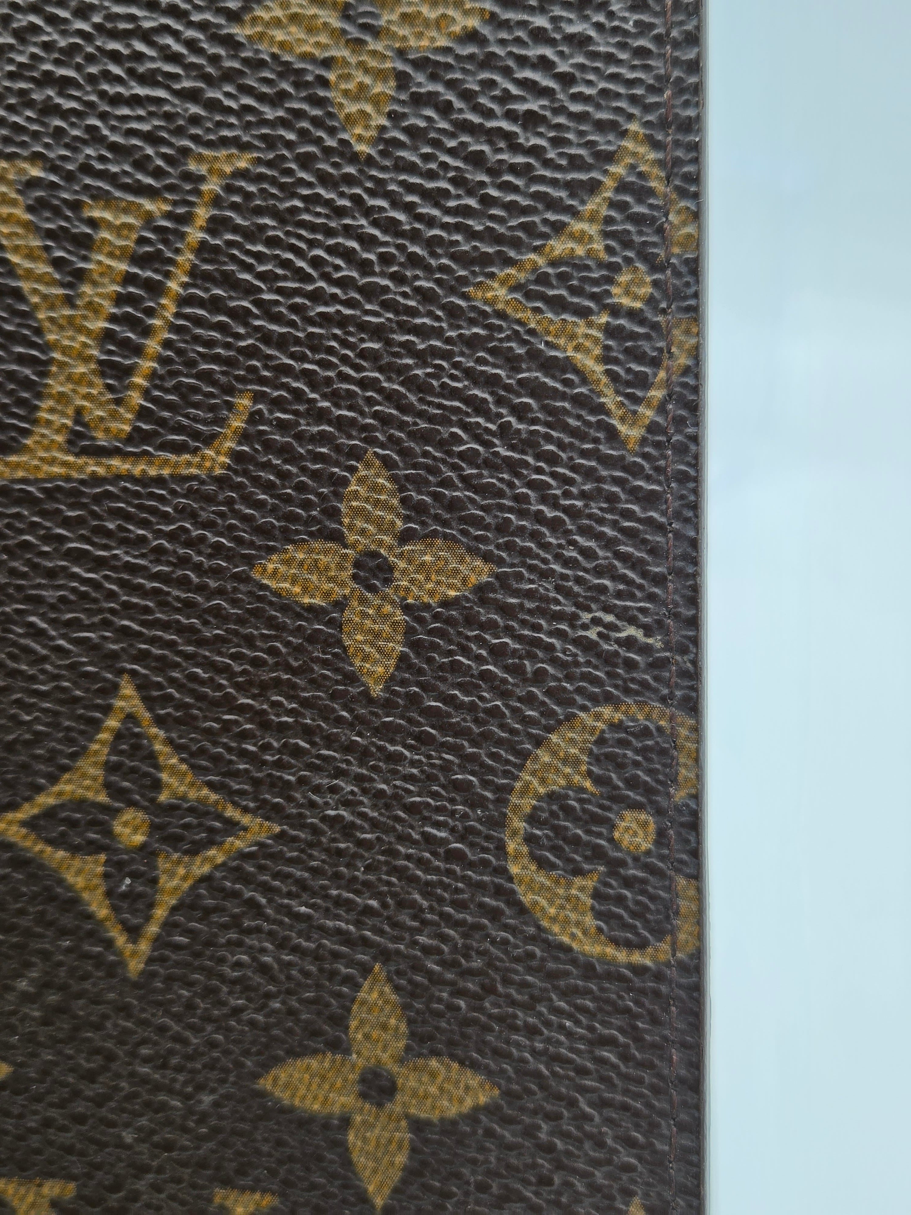 Close-up of Louis Vuitton monogram canvas with brown textured background and tan/golden LV and floral motifs, shown against a pale blue background.