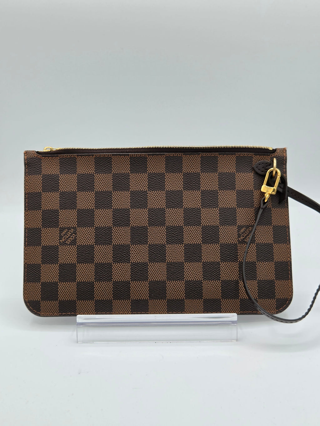 A brown and dark brown checkerboard clutch bag with gold-tone hardware, shown hanging against a light gray background.