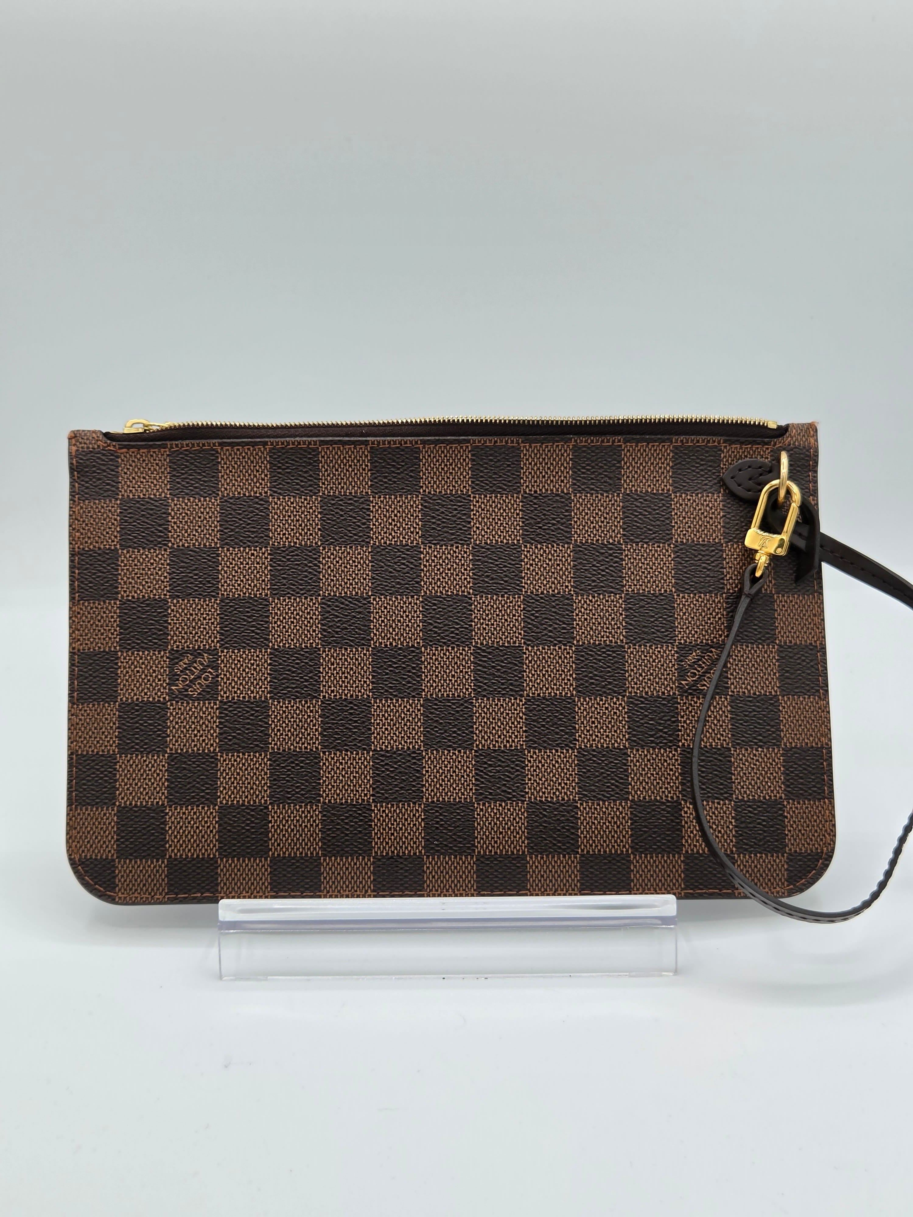A brown and dark brown checkerboard clutch bag with gold-tone hardware, shown hanging against a light gray background.