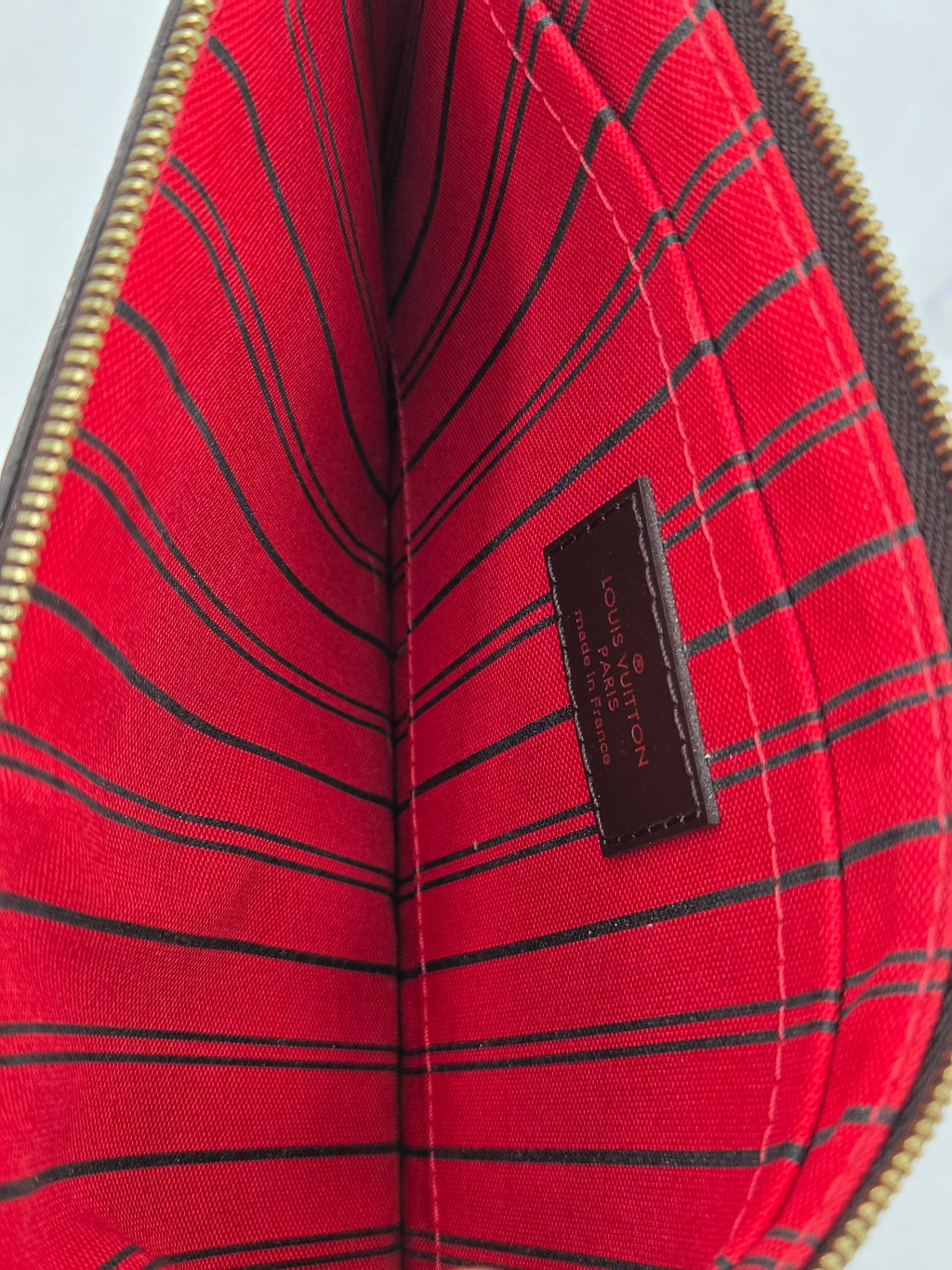 Close-up of the interior lining of a Louis Vuitton pouch or wallet, featuring a vibrant red fabric with thin black vertical stripes and a brown leather brand label stitched in the center.