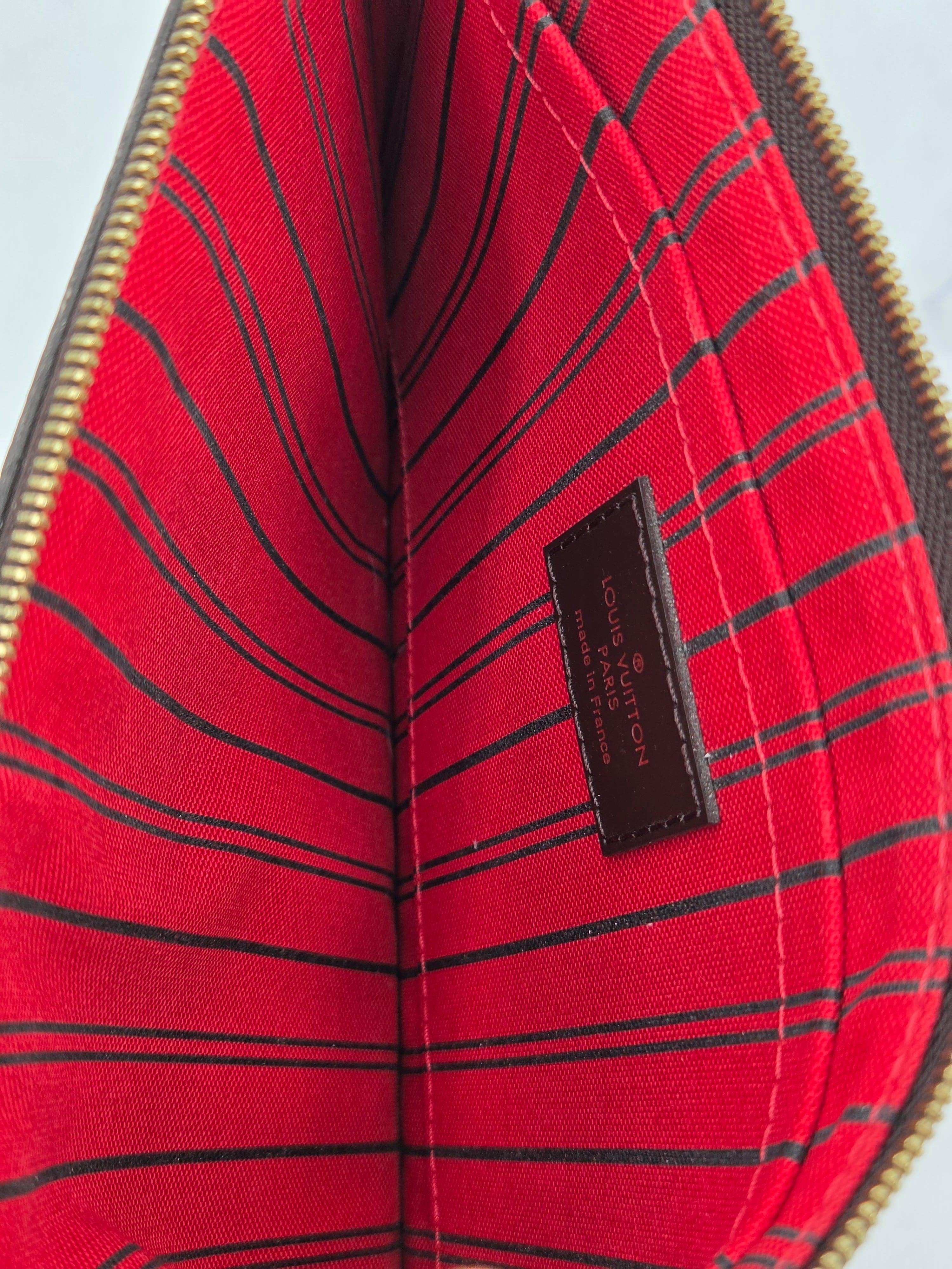 Close-up of the interior lining of a Louis Vuitton pouch or wallet, featuring a vibrant red fabric with thin black vertical stripes and a brown leather brand label stitched in the center.