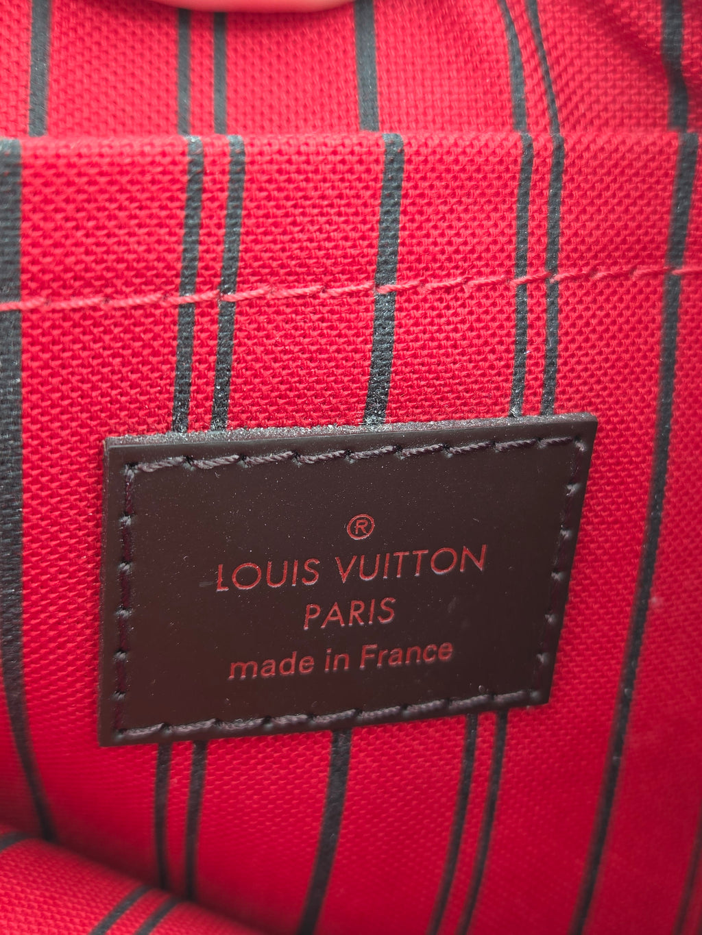 Close-up of a Louis Vuitton patch on red and black striped fabric, with the text 'LOUIS VUITTON PARIS made in France' visible.