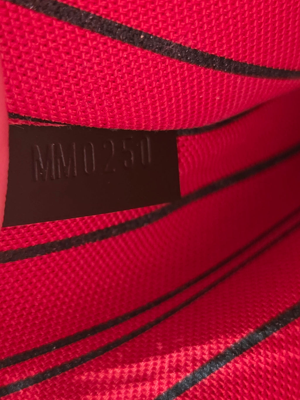 Close-up of a red textured fabric with black stripes and a dark brown rectangular label embossed with 'MM0251'.