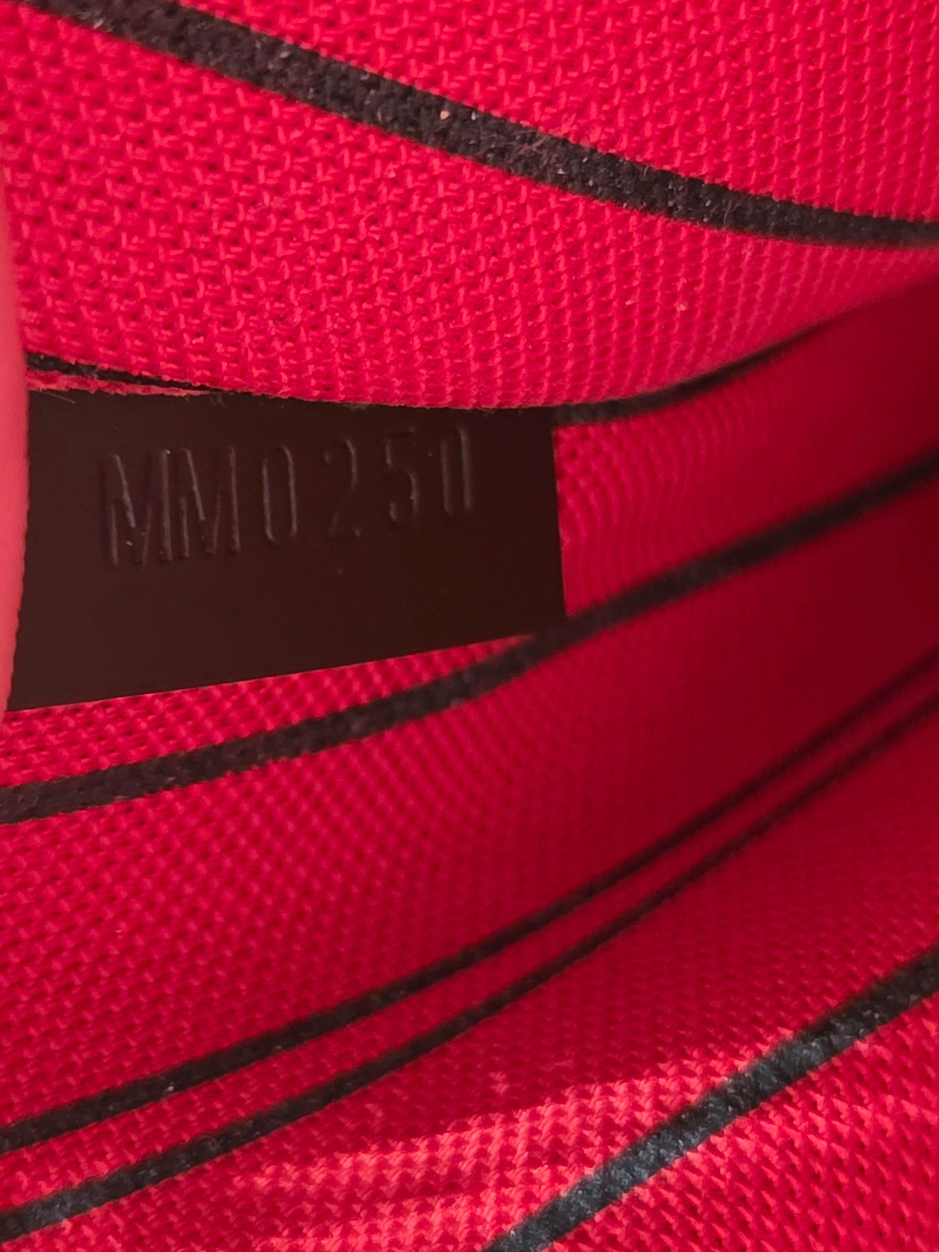Close-up of a red textured fabric with black stripes and a dark brown rectangular label embossed with 'MM0251'.