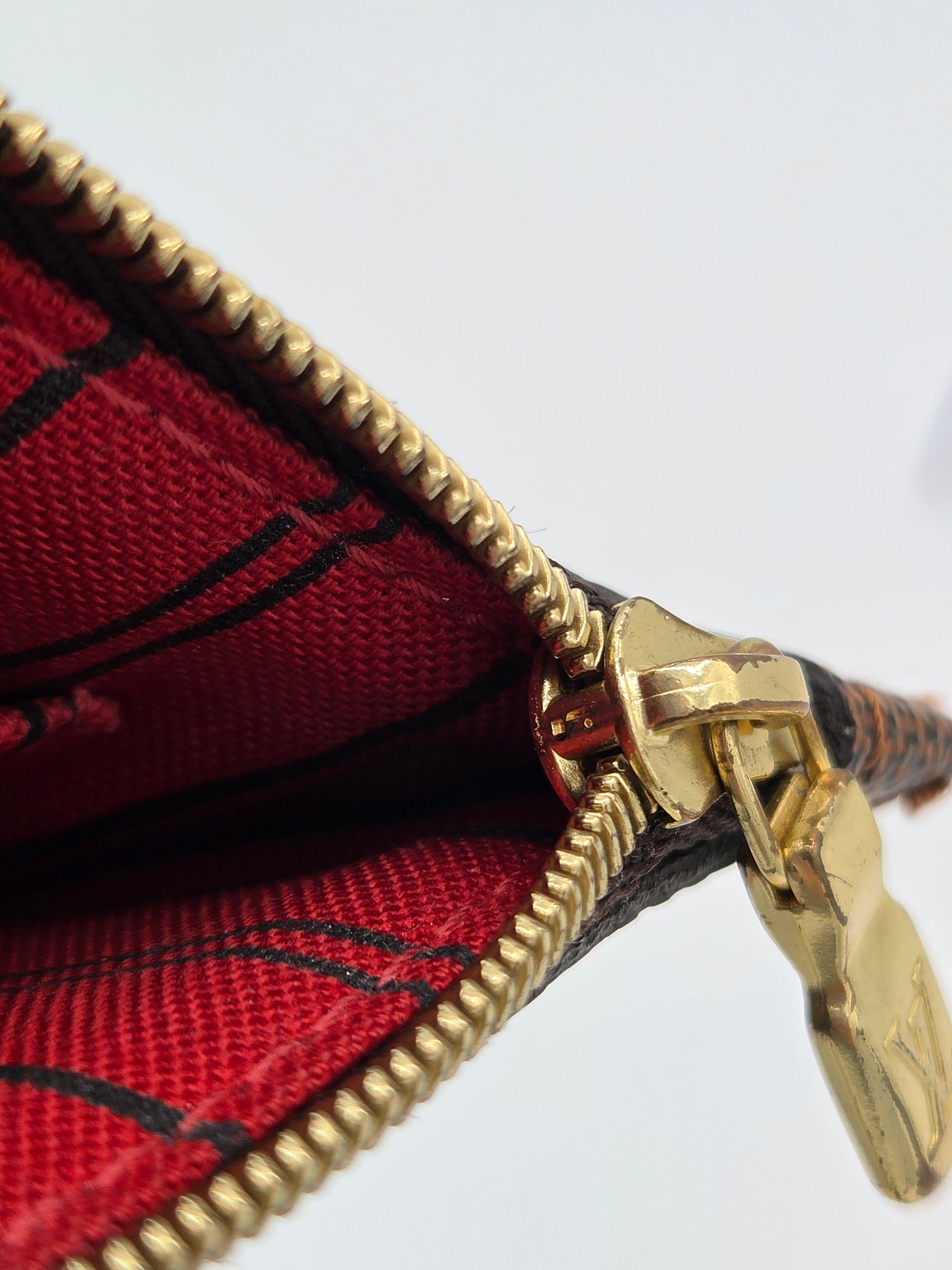 Close-up of a red plaid fabric pouch or wallet with a gold zipper and gold pull tab, shown against a plain white background.