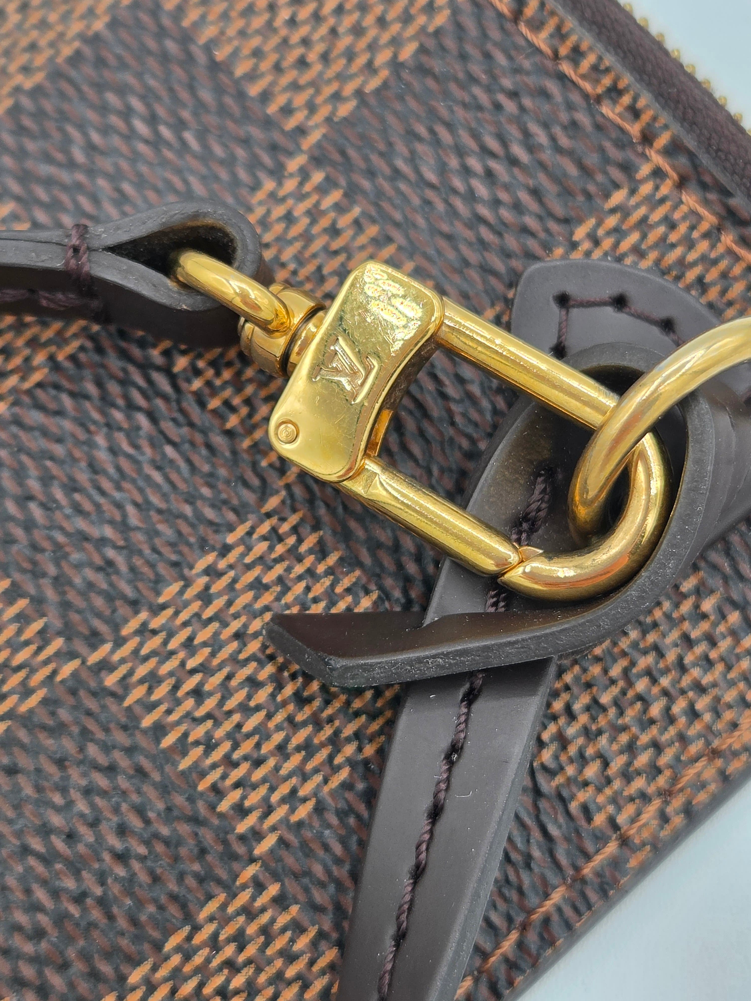 Close-up of a Louis Vuitton monogram bag featuring a gold-tone metal clasp with the LV logo, dark brown leather strap, and the classic dark brown and tan checkered canvas.