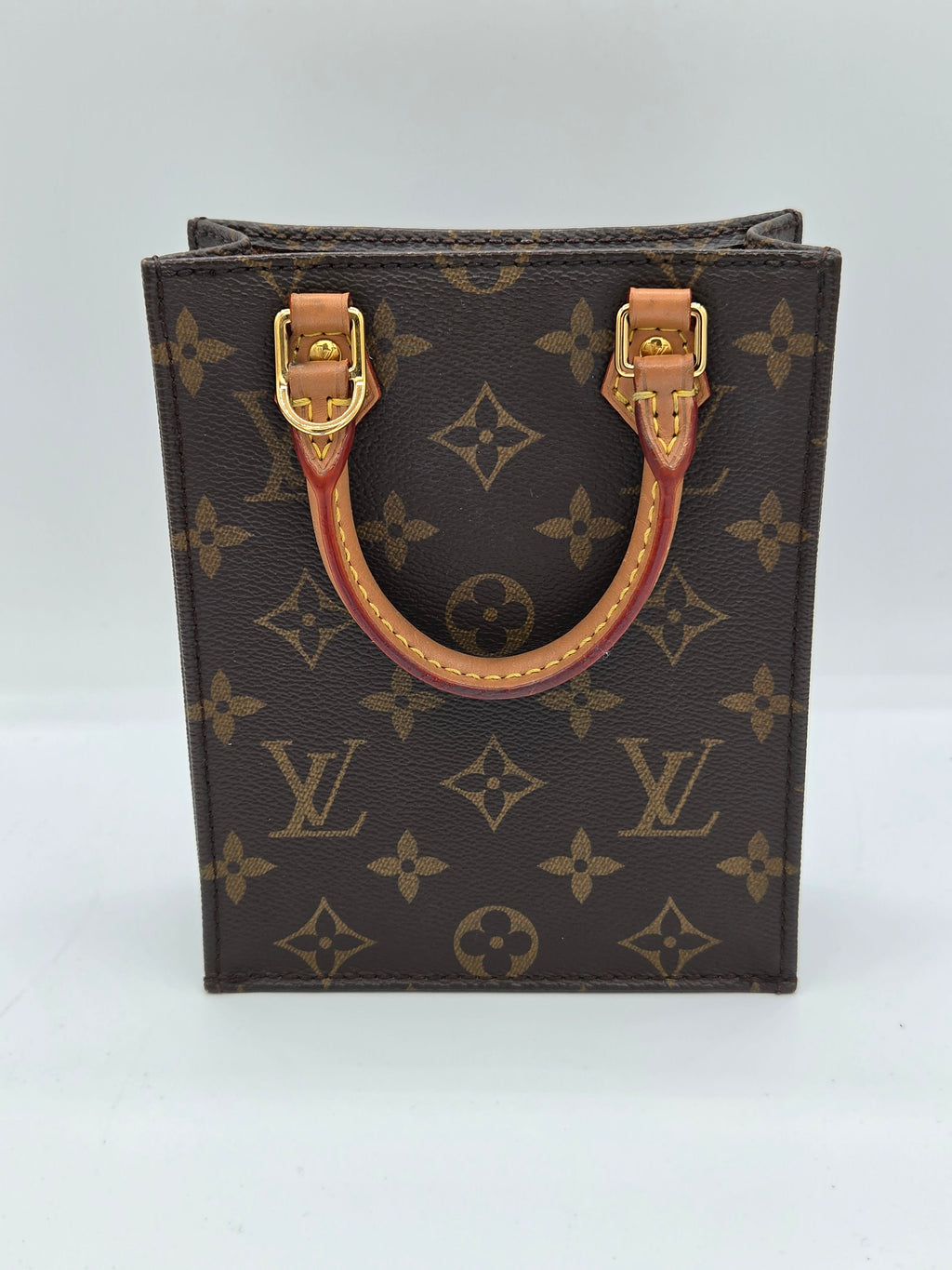 A Louis Vuitton monogram canvas top-handle pouch or small bag, shown from above on a plain white background. The dark brown coated canvas features the classic tan monogram pattern, with a tan leather handle and gold-tone hardware.