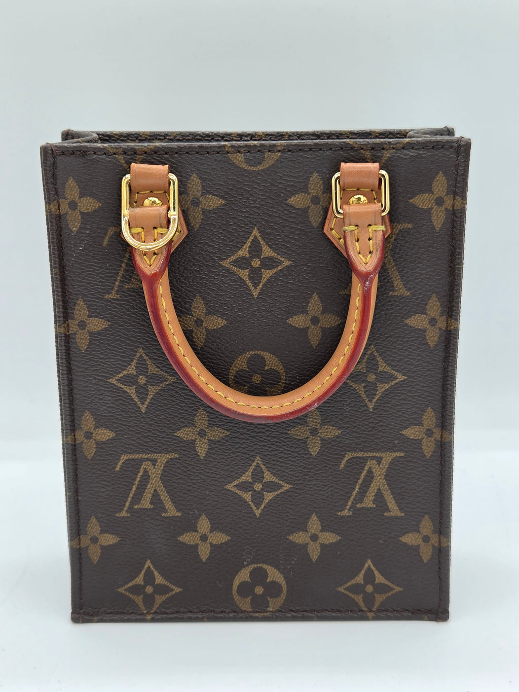 A Louis Vuitton monogram canvas card holder or small wallet with a curved tan leather handle and gold-tone hardware, shown against a plain light background.