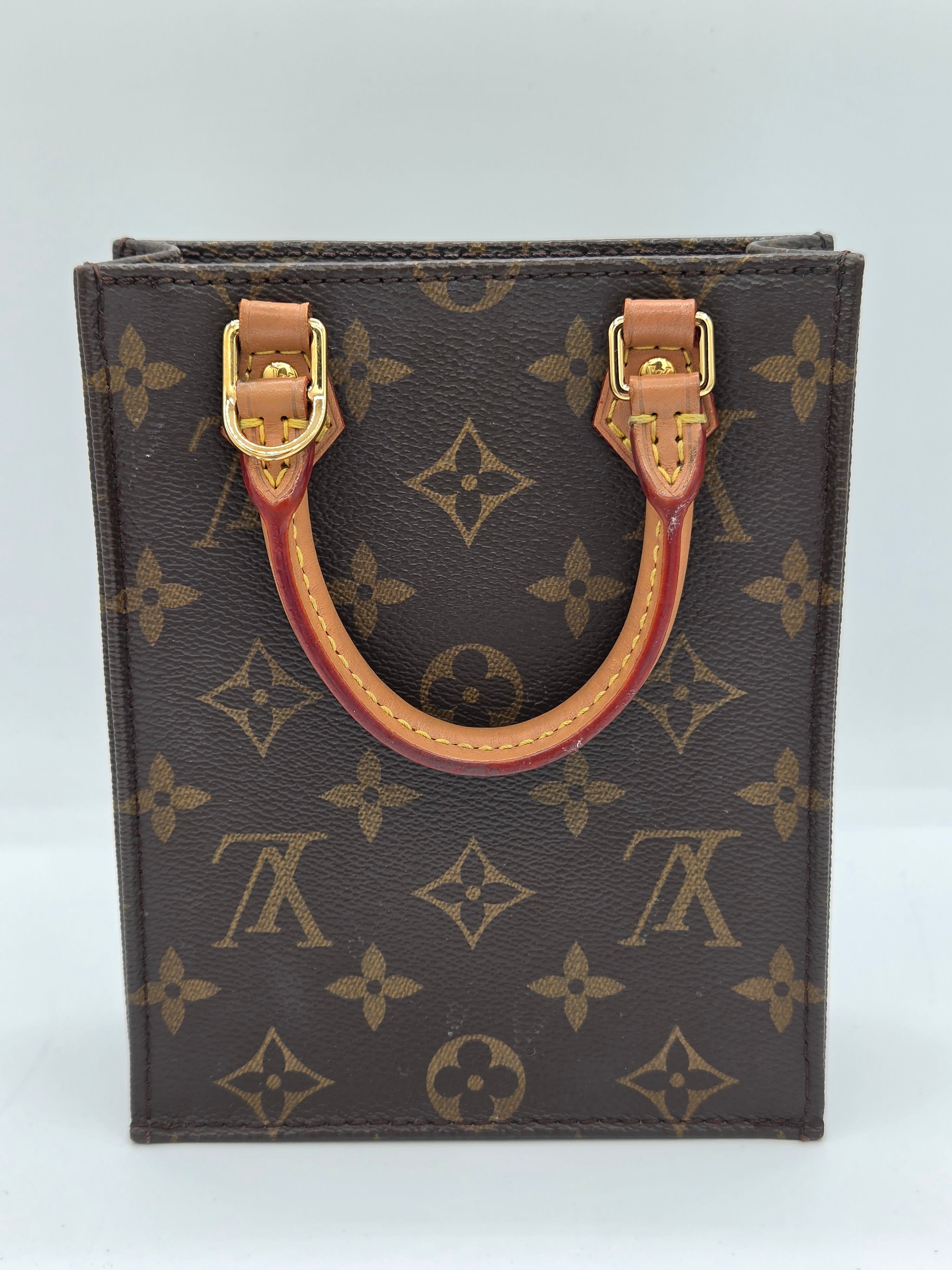 A Louis Vuitton monogram canvas card holder or small wallet with a curved tan leather handle and gold-tone hardware, shown against a plain light background.