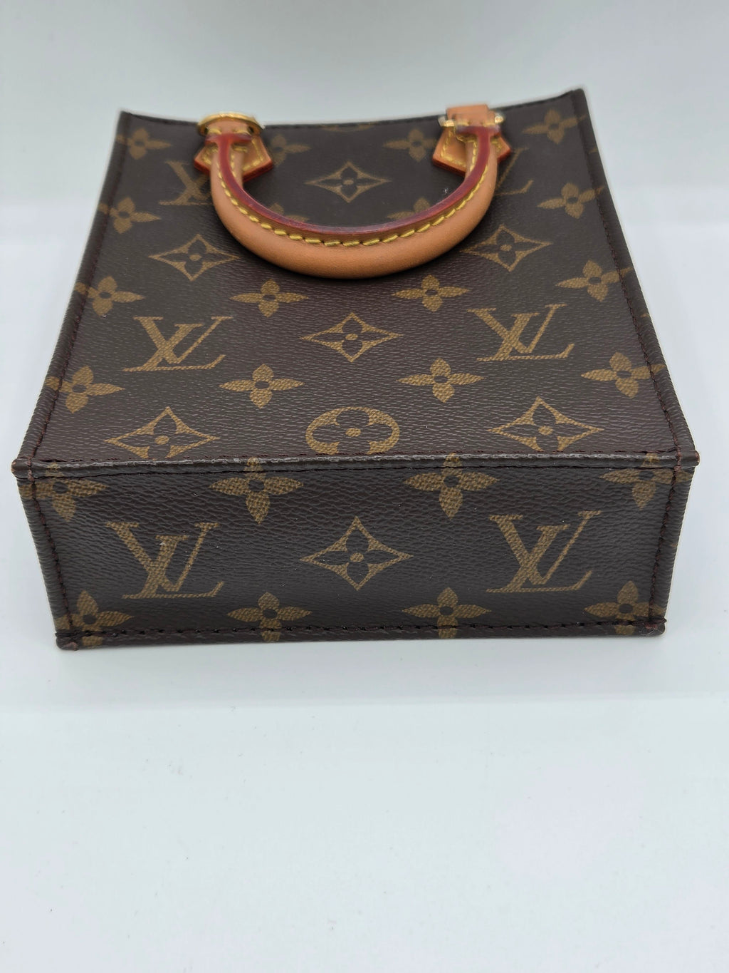 Louis Vuitton monogram canvas handbag with a tan leather handle, shown against a plain white background.