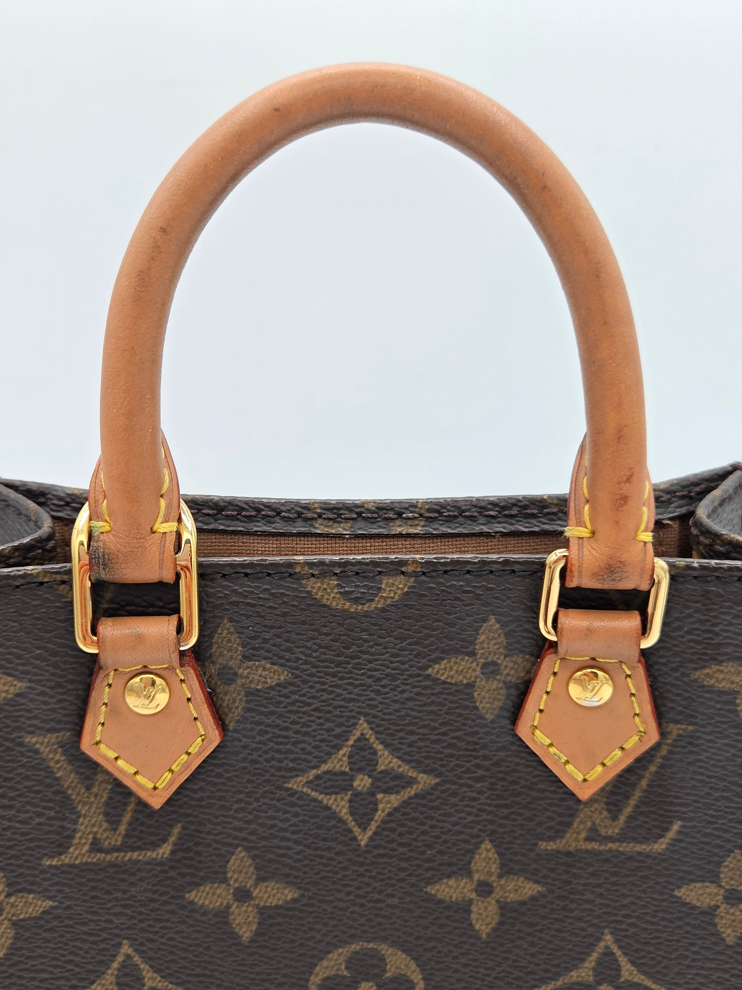 Close-up of a Louis Vuitton monogram handbag showing a curved tan leather handle attached to dark brown coated canvas with gold-tone hardware and the repeating LV monogram pattern.